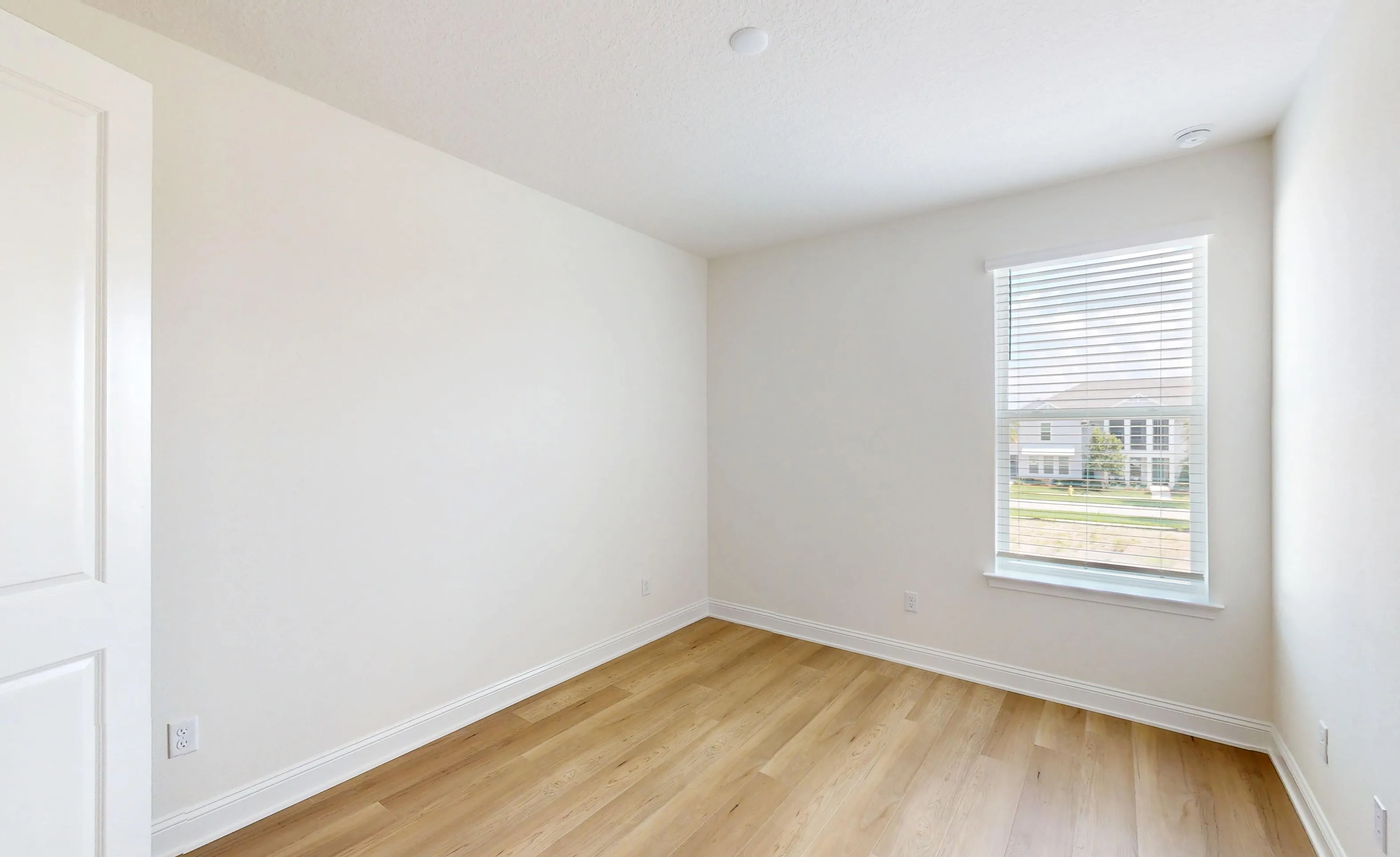 Secondary bedroom with light wood-style flooring, white walls, and a window with white horizontal blinds.