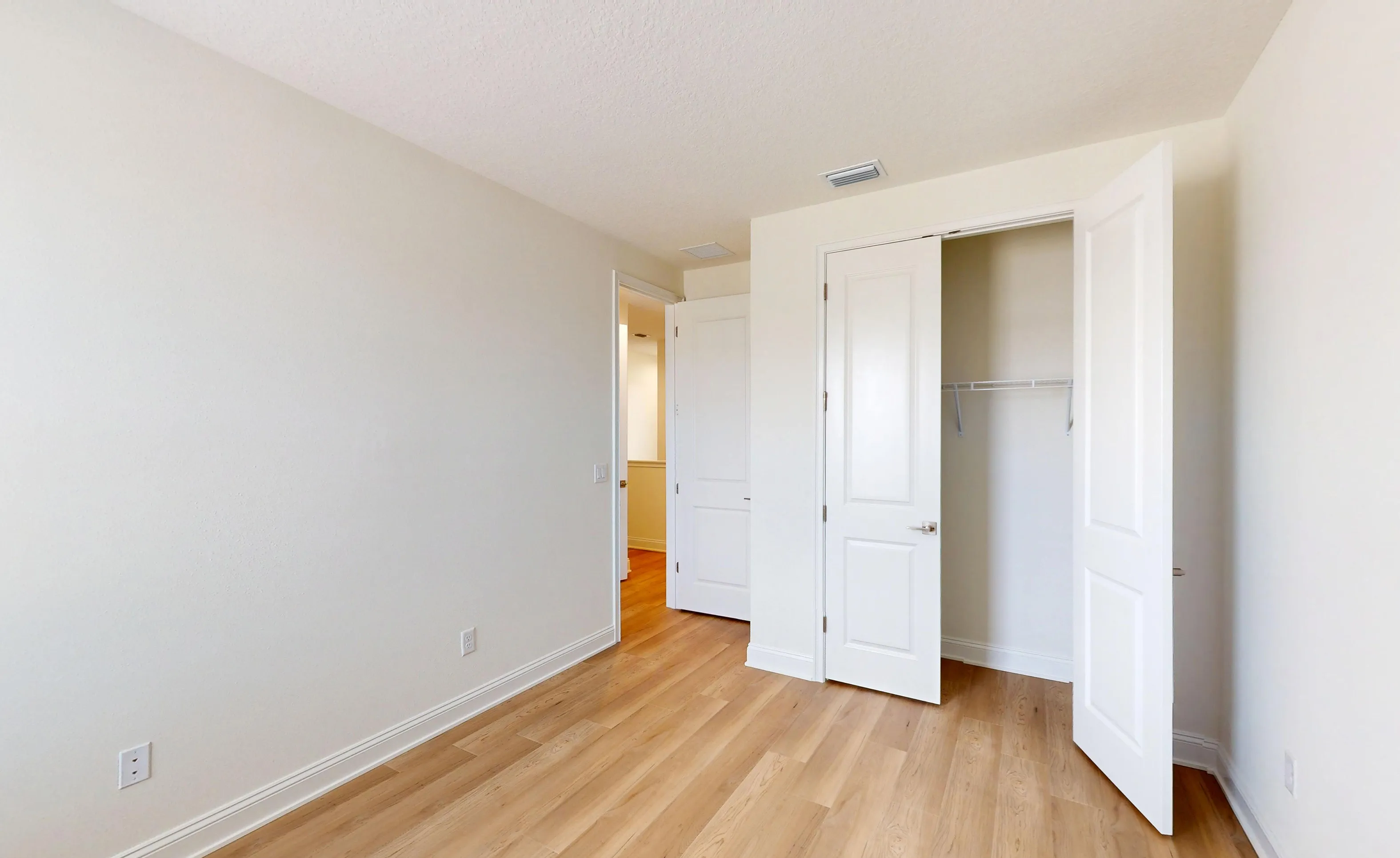 Secondary bedroom in the Castillo floor plan with light wood-style flooring, white walls, and a walk-in closet.