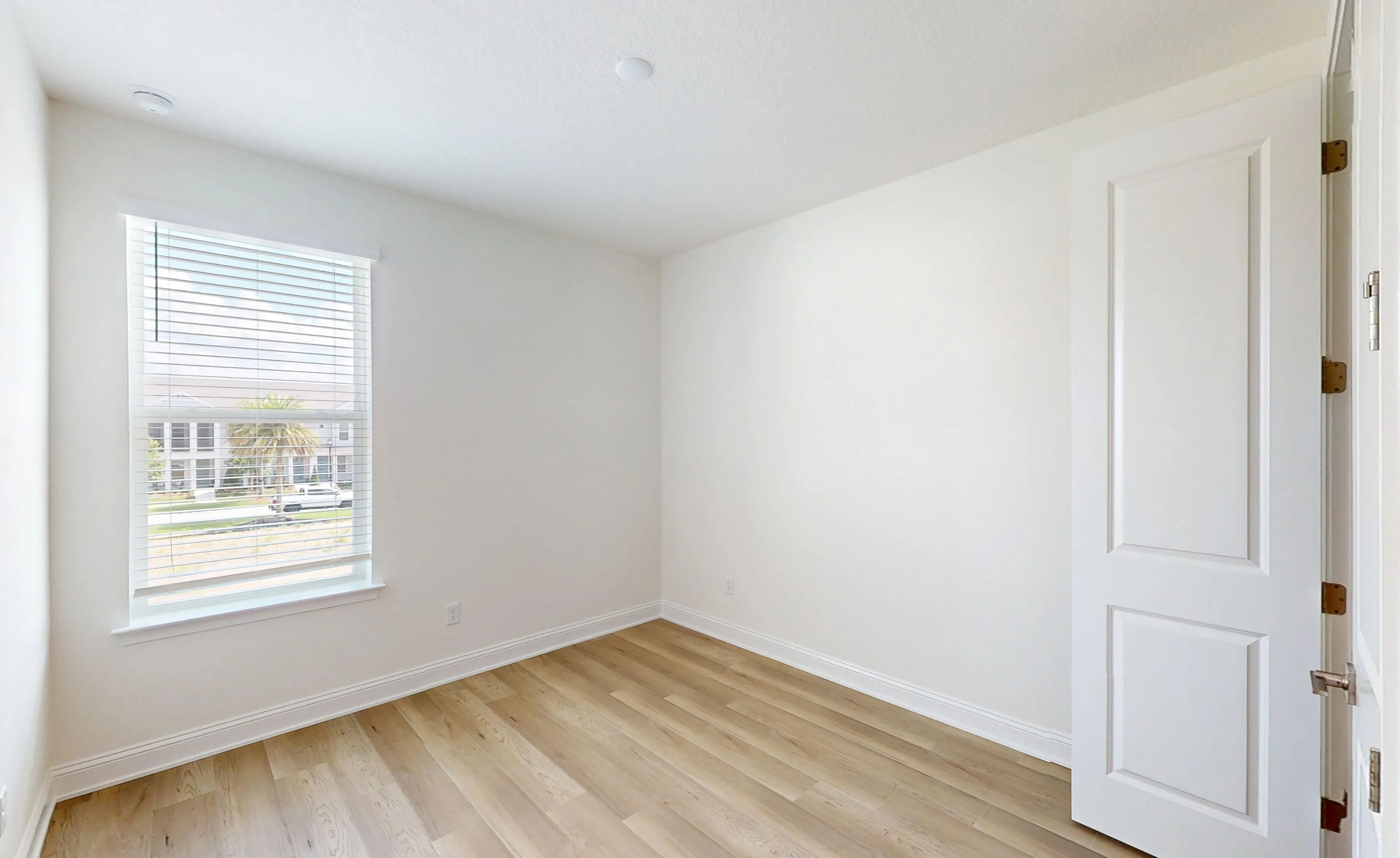 Secondary bedroom in the Castillo floor plan with white walls, light wood-style flooring, and a single window with blinds.