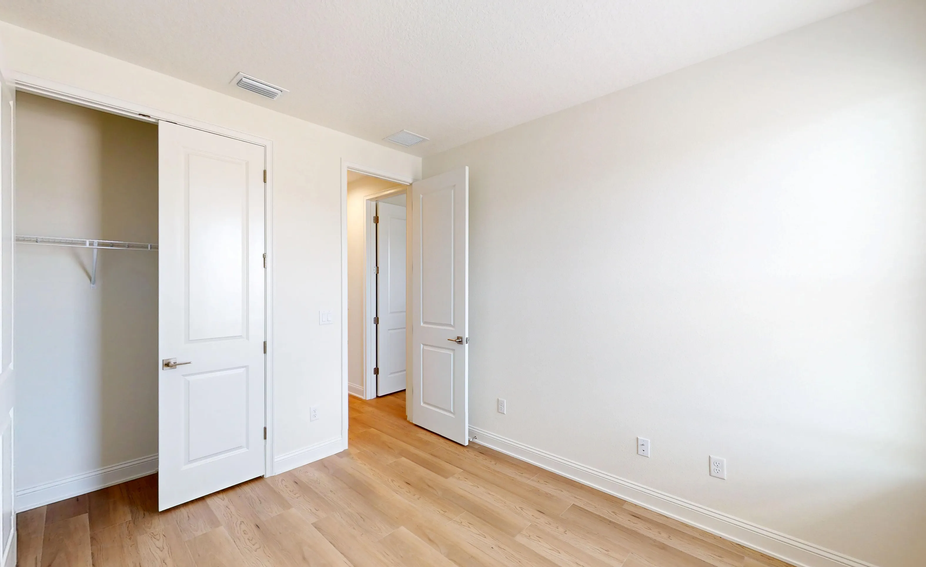 Secondary bedroom with light wood flooring, white walls, white doors, a closet with wire shelving, and an open doorway.