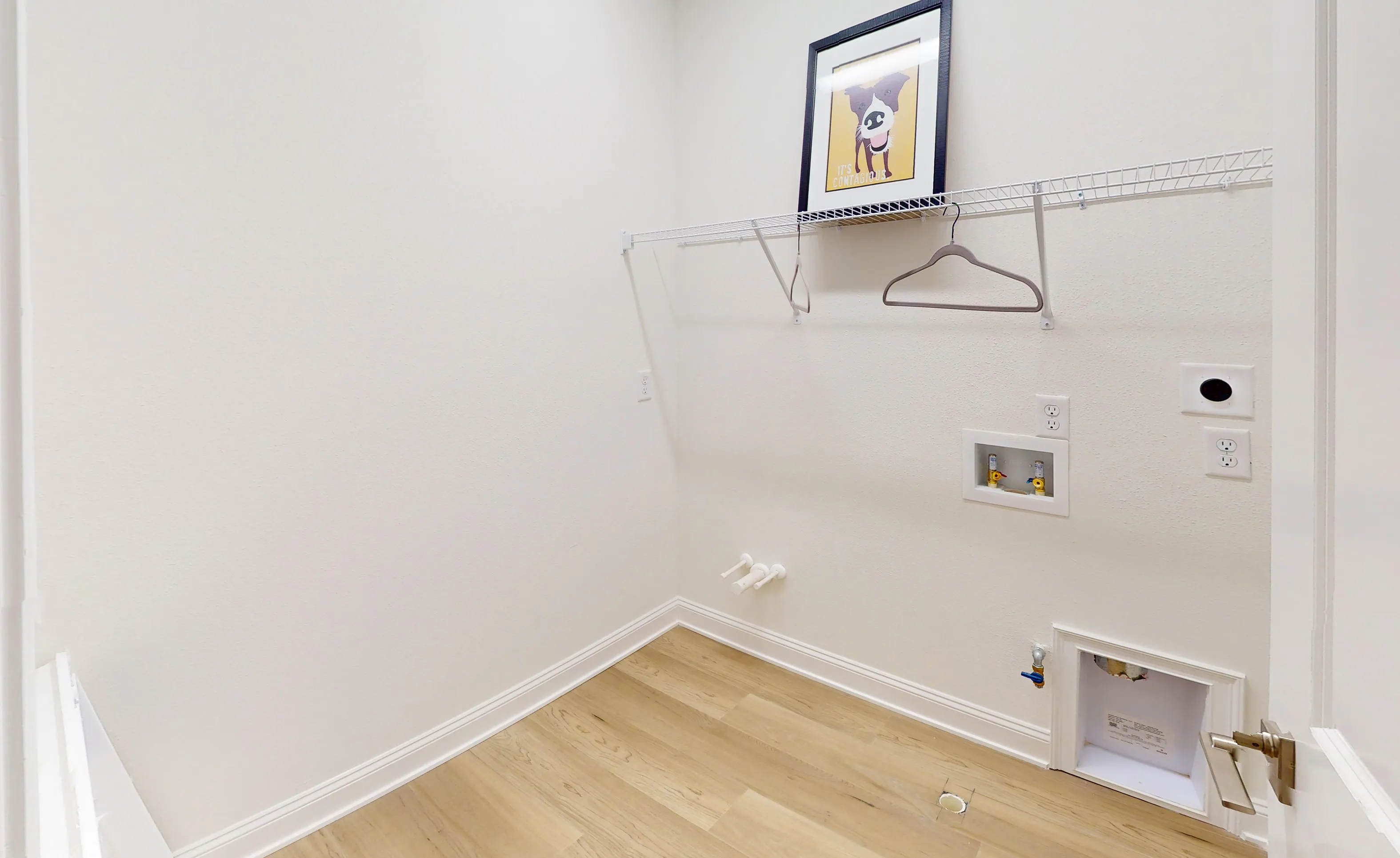 Laundry room in the Castillo plan with light wood flooring, white walls, wire shelving, and appliance hookups.