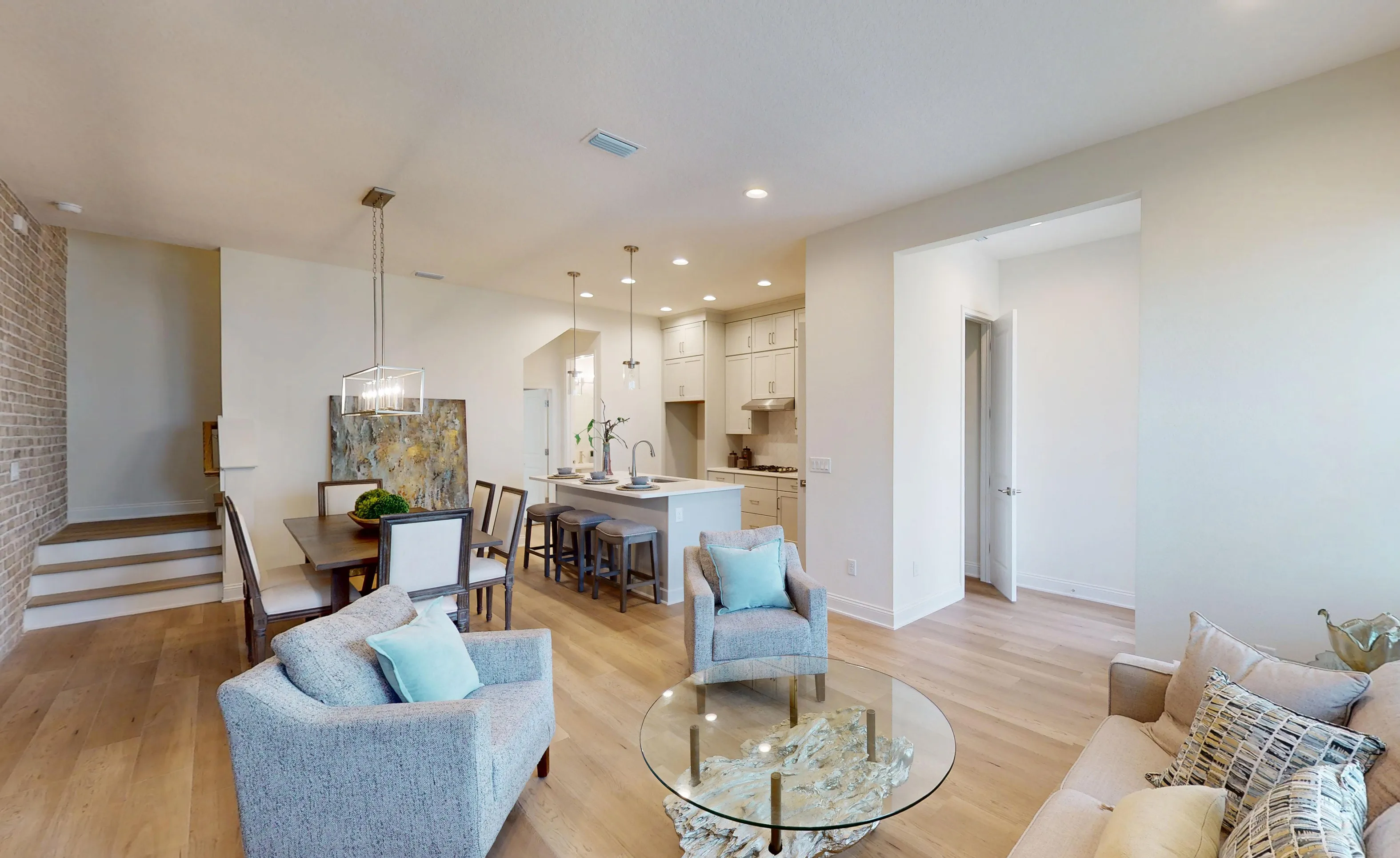 Open-concept living room and dining area in the Castillo floor plan with hardwood floors, a kitchen island, and brick wall.