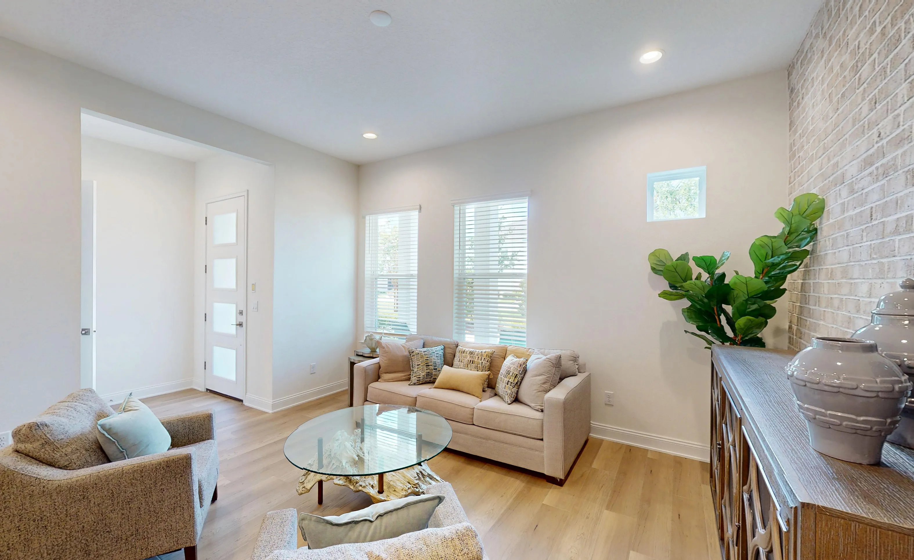 Living room in the Castillo plan featuring a light brick accent wall, light wood flooring, a sofa, and an armchair.
