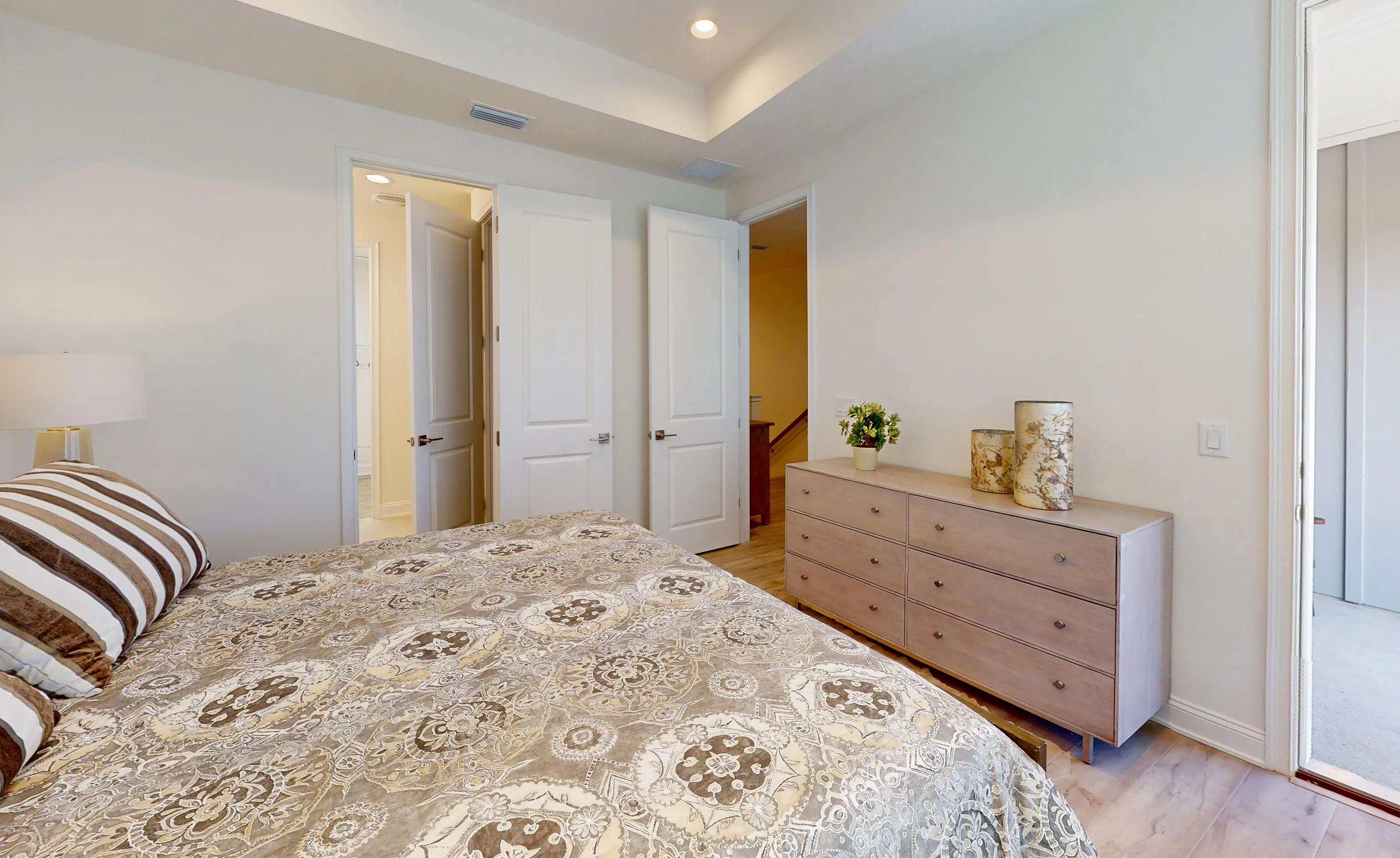 Primary bedroom of the Deleon plan featuring a tray ceiling, wood-look flooring, two interior doors, and a dresser.
