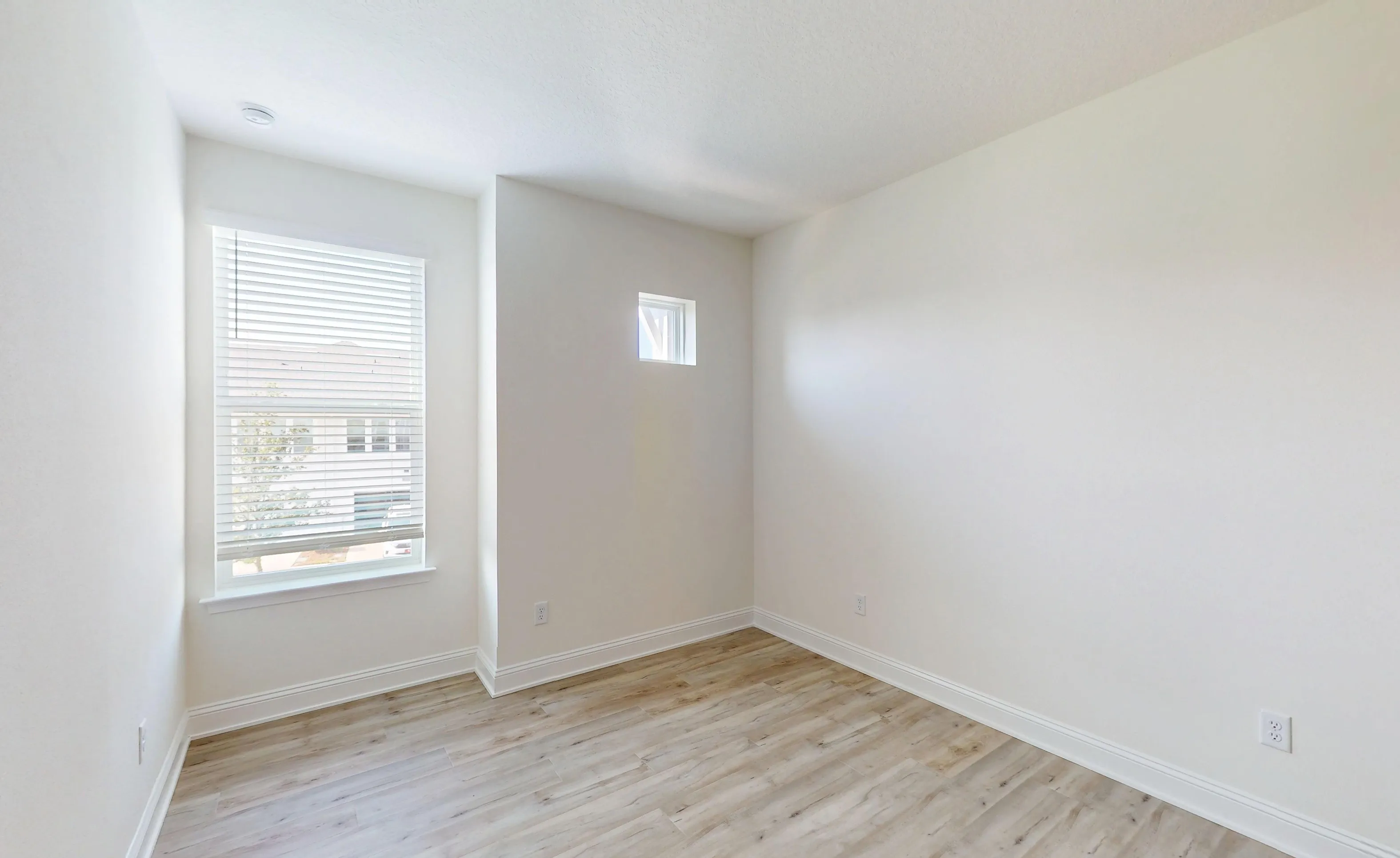 Secondary bedroom in Nocatee with light wood-look flooring, white walls, a large window with blinds, and a small square window.