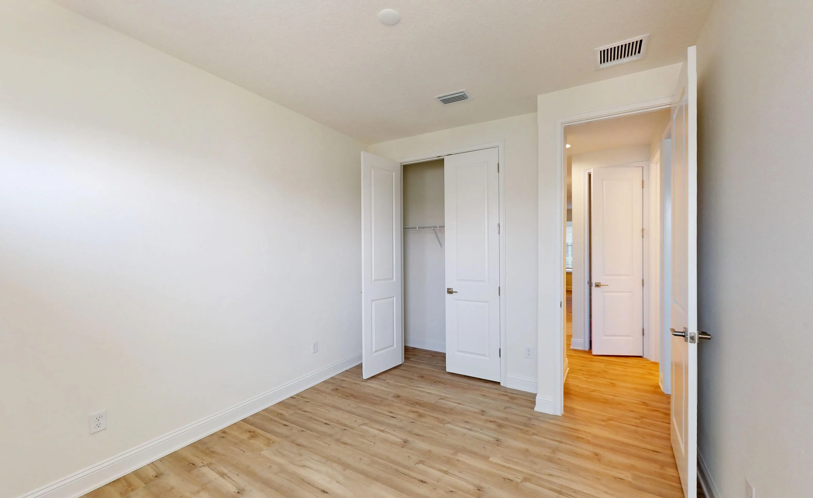 Secondary bedroom in the Deleon plan with white walls, light wood-look flooring, an open closet, and an open doorway.