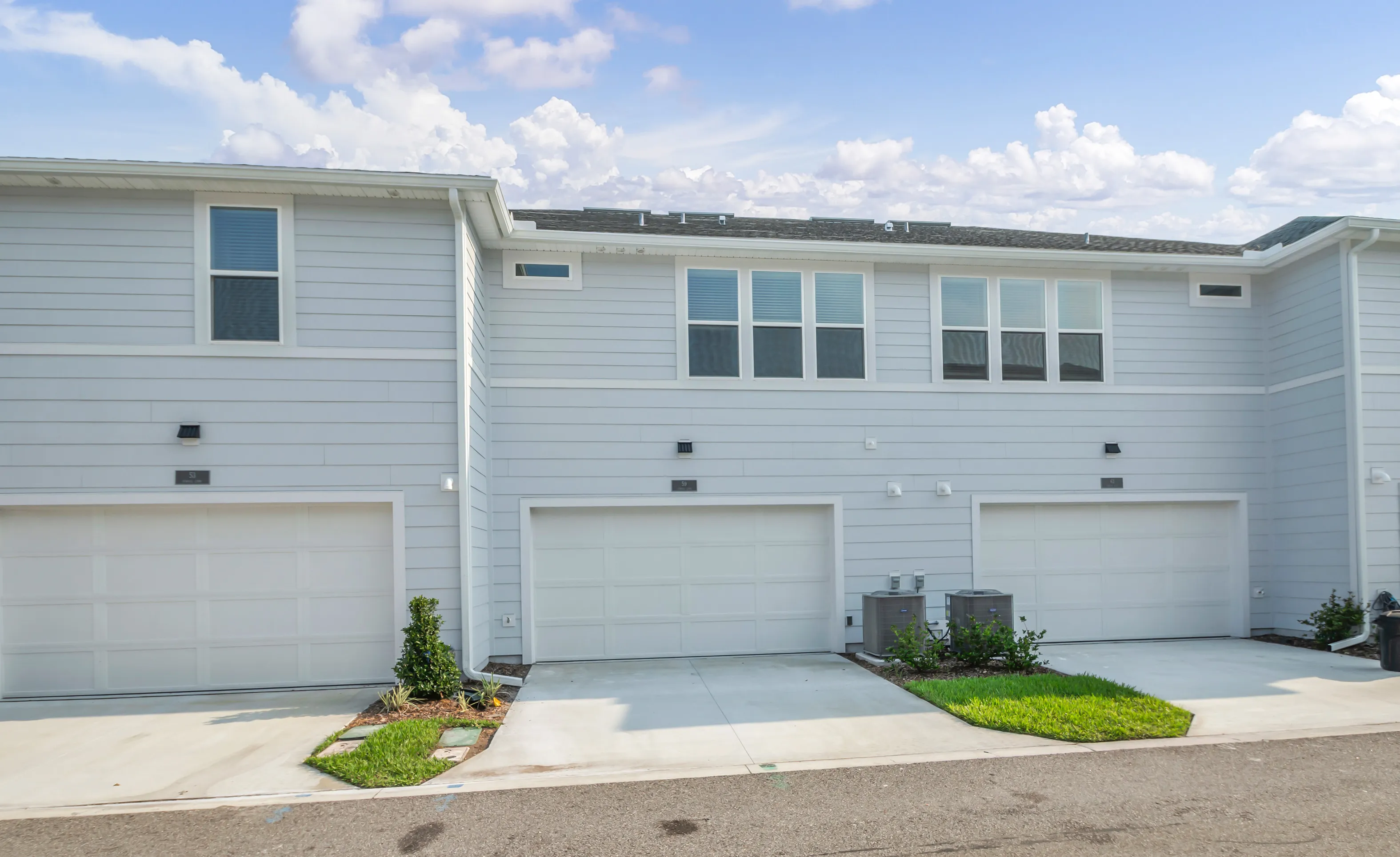 Rear exterior of light blue townhouse units in Nocatee with three white garage doors and concrete driveways.