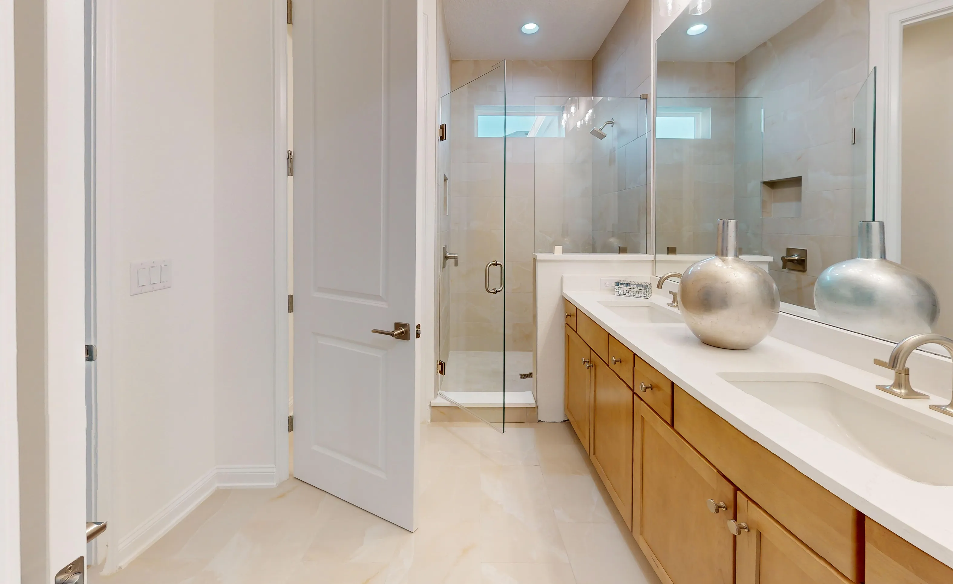 Primary bathroom with light wood dual vanity, white countertops, a large mirror, and a glass-enclosed walk-in tile shower.
