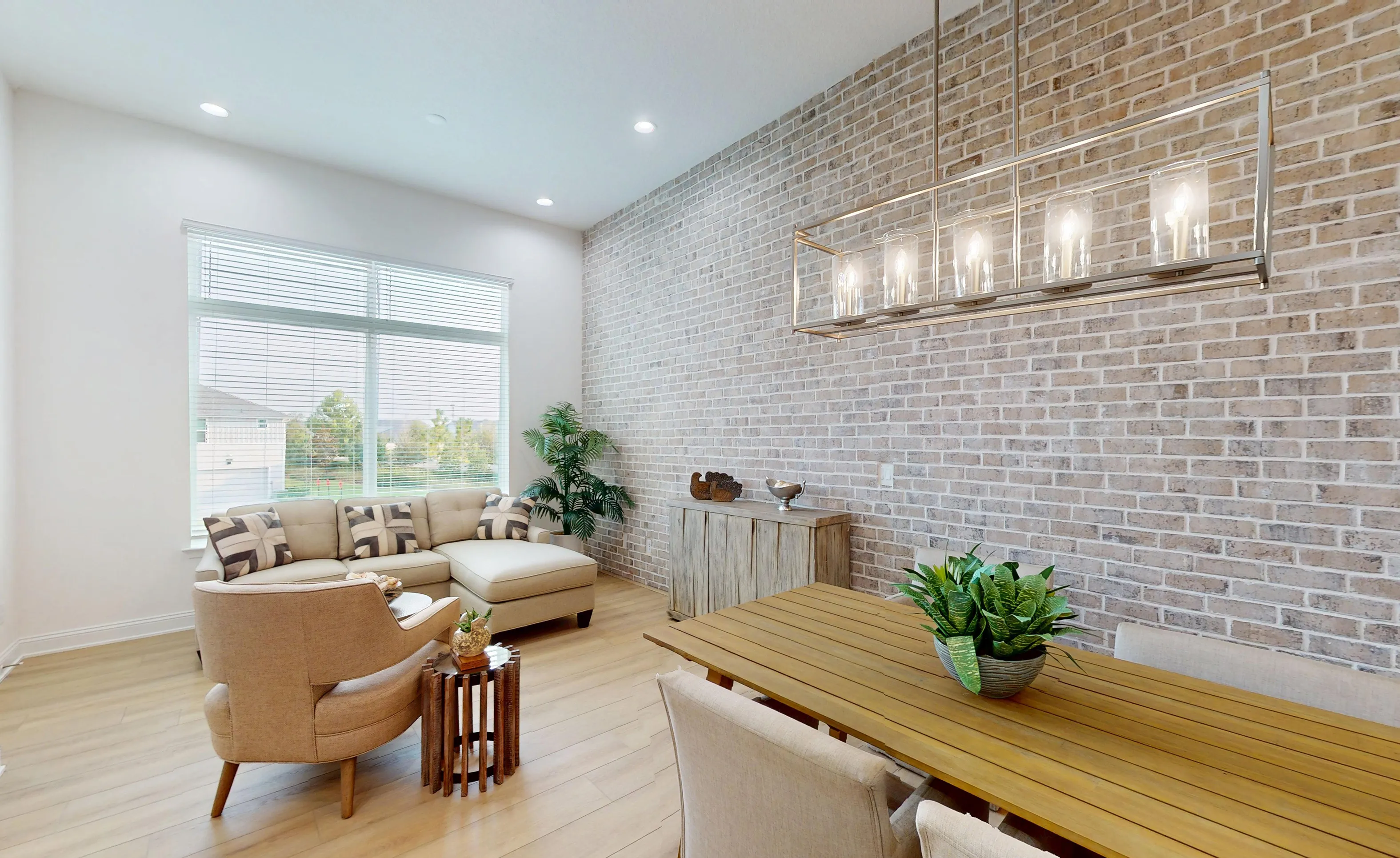 Dining room in the Gulf plan featuring light wood floors, a brick accent wall, a rectangular chandelier, and neutral furniture.