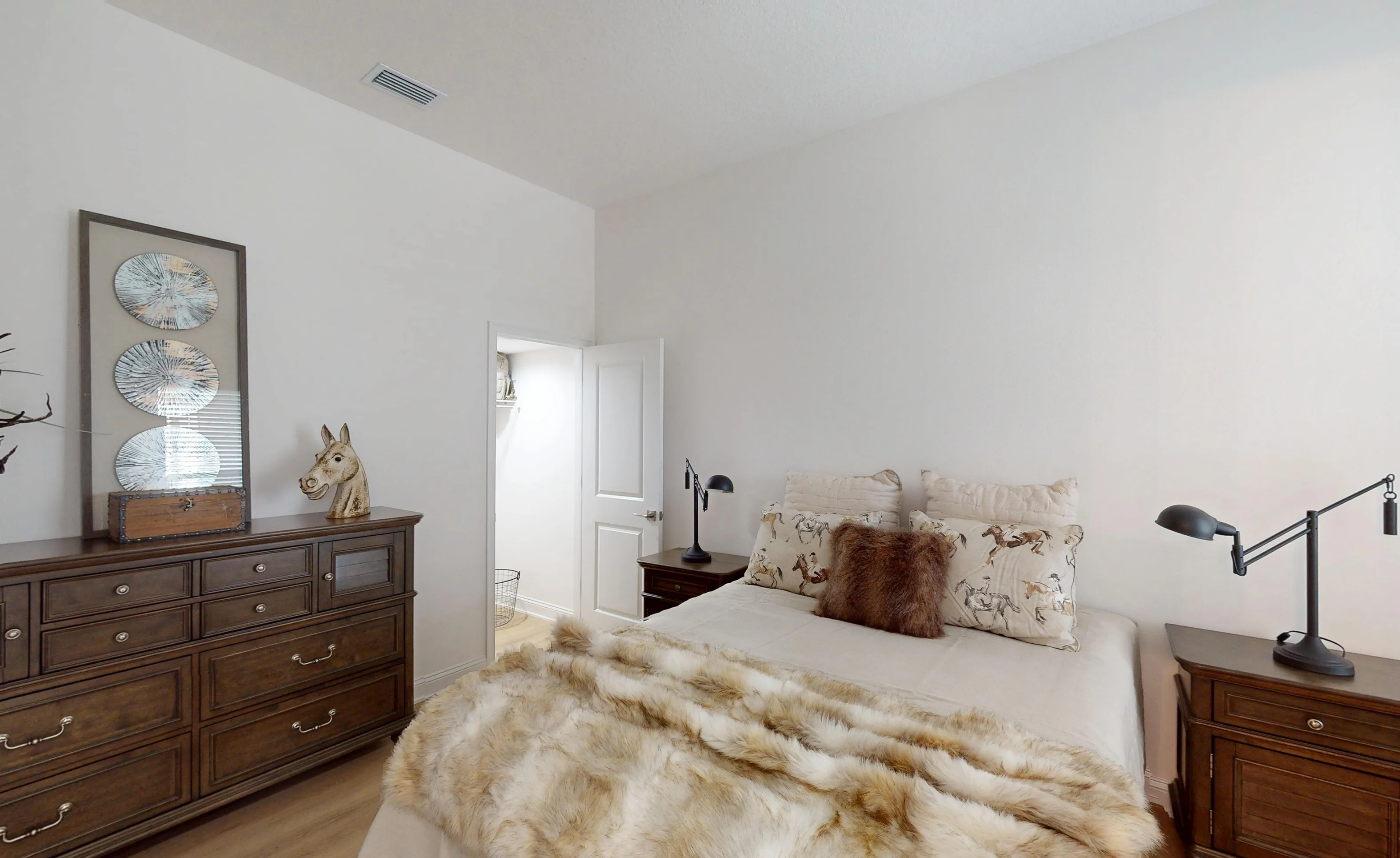 Secondary bedroom in the Gulf plan featuring a bed with a faux fur throw, matching wood furniture, and an open closet door.