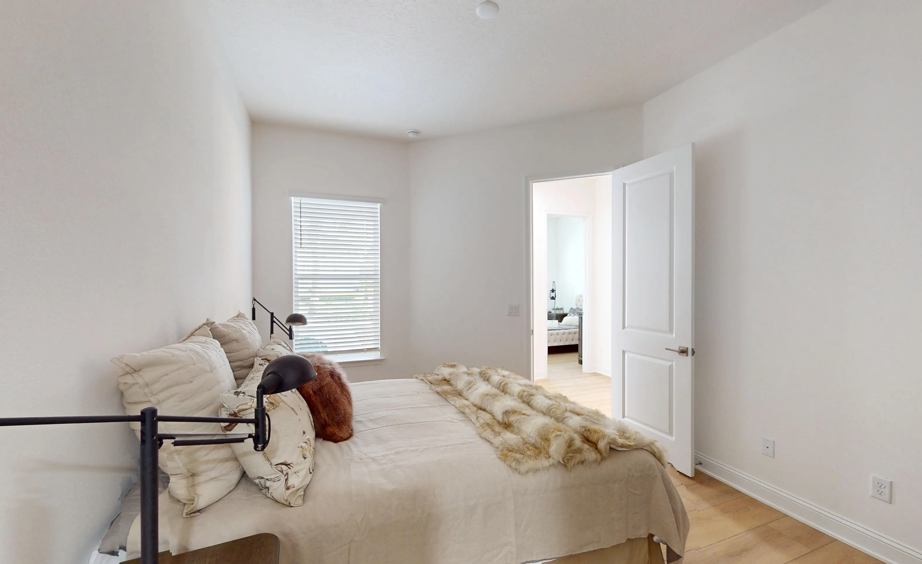 Secondary bedroom with a bed, wood-look flooring, a window with blinds, and an open doorway leading to another room.
