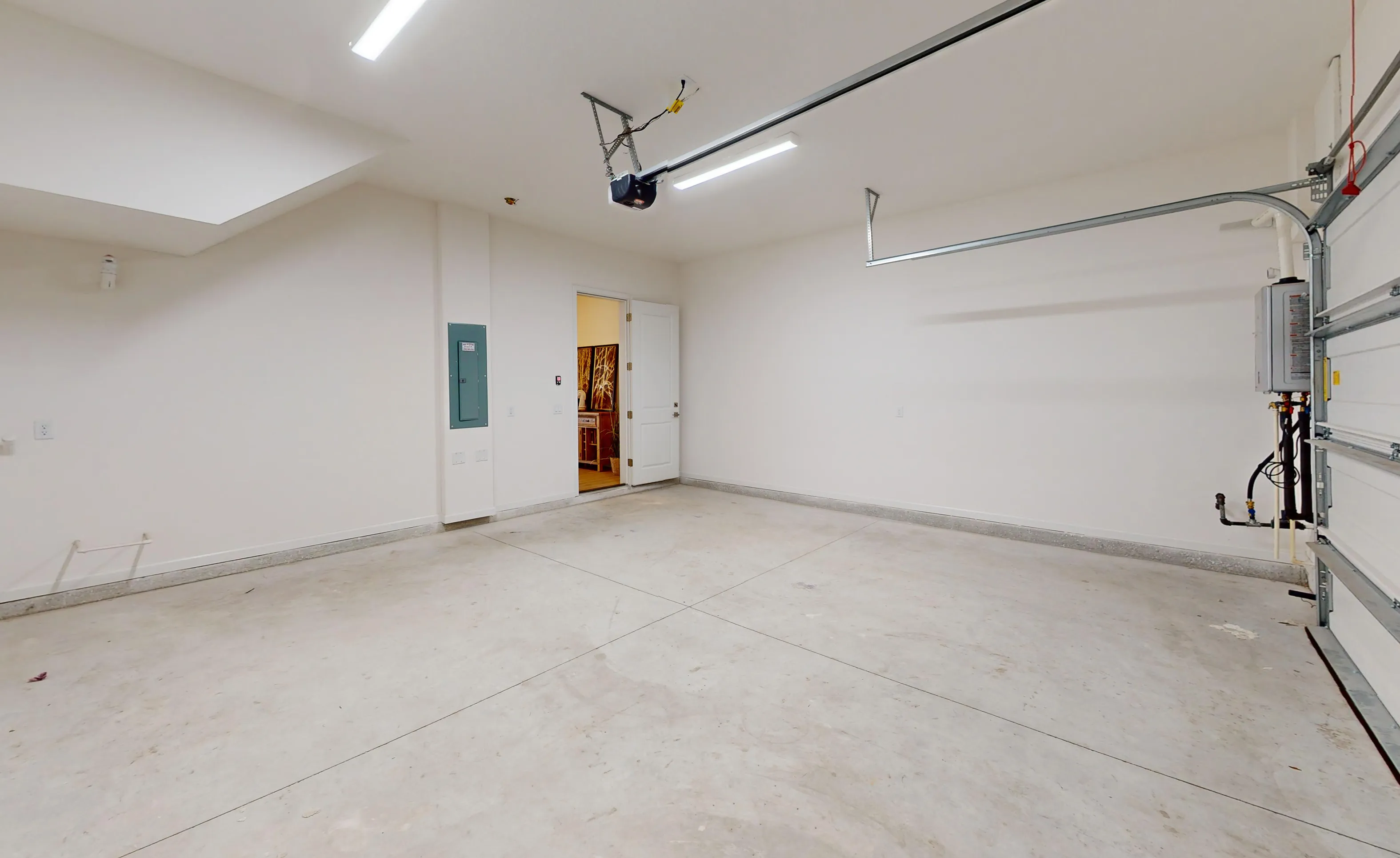 Unfinished garage with concrete floor, white walls, electrical panel, and a doorway leading into the home.