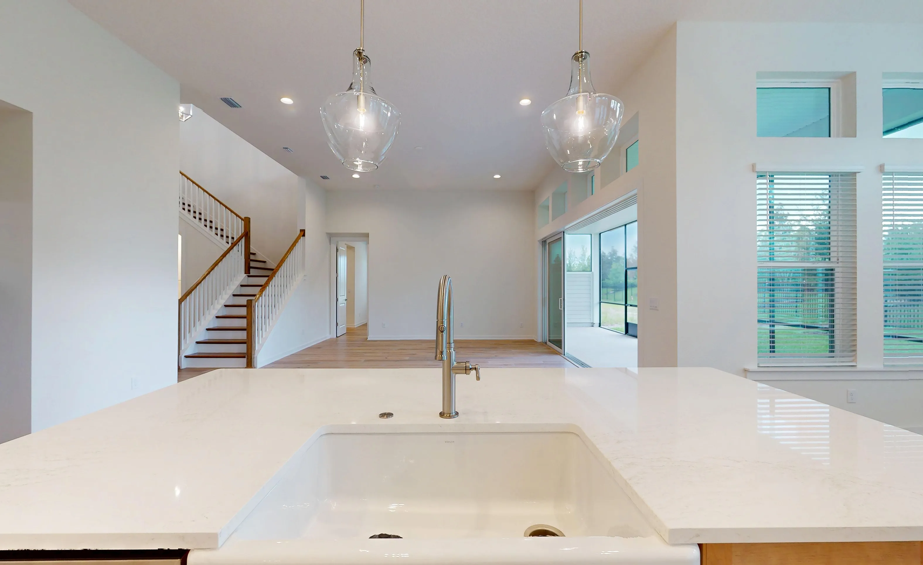 Kitchen island with white farmhouse sink and faucet, overlooking a spacious living area, staircase, and outdoor patio.