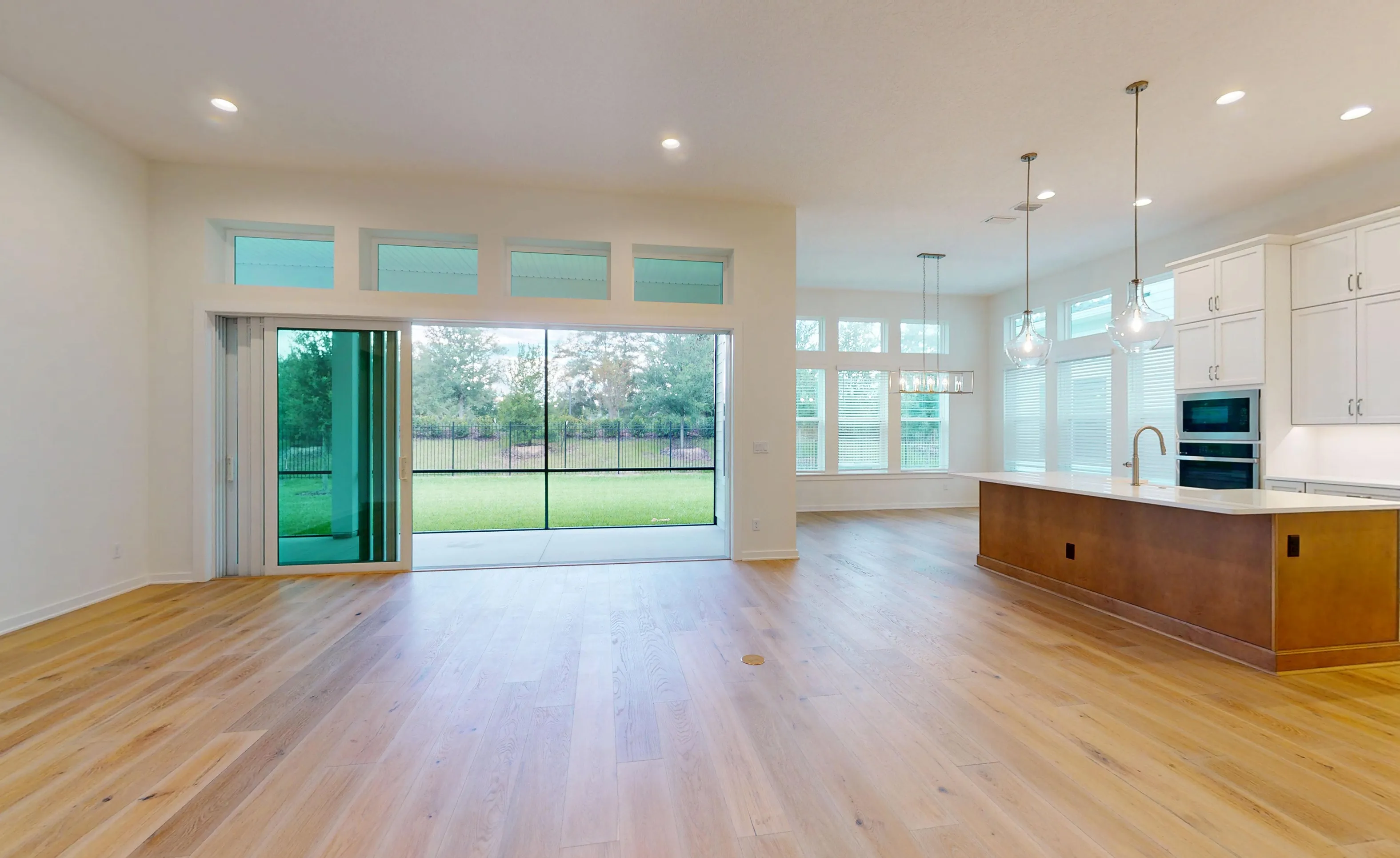 Open living room and kitchen in Palos Verdes plan, featuring hardwood floors, sliding glass doors to a backyard, and island.