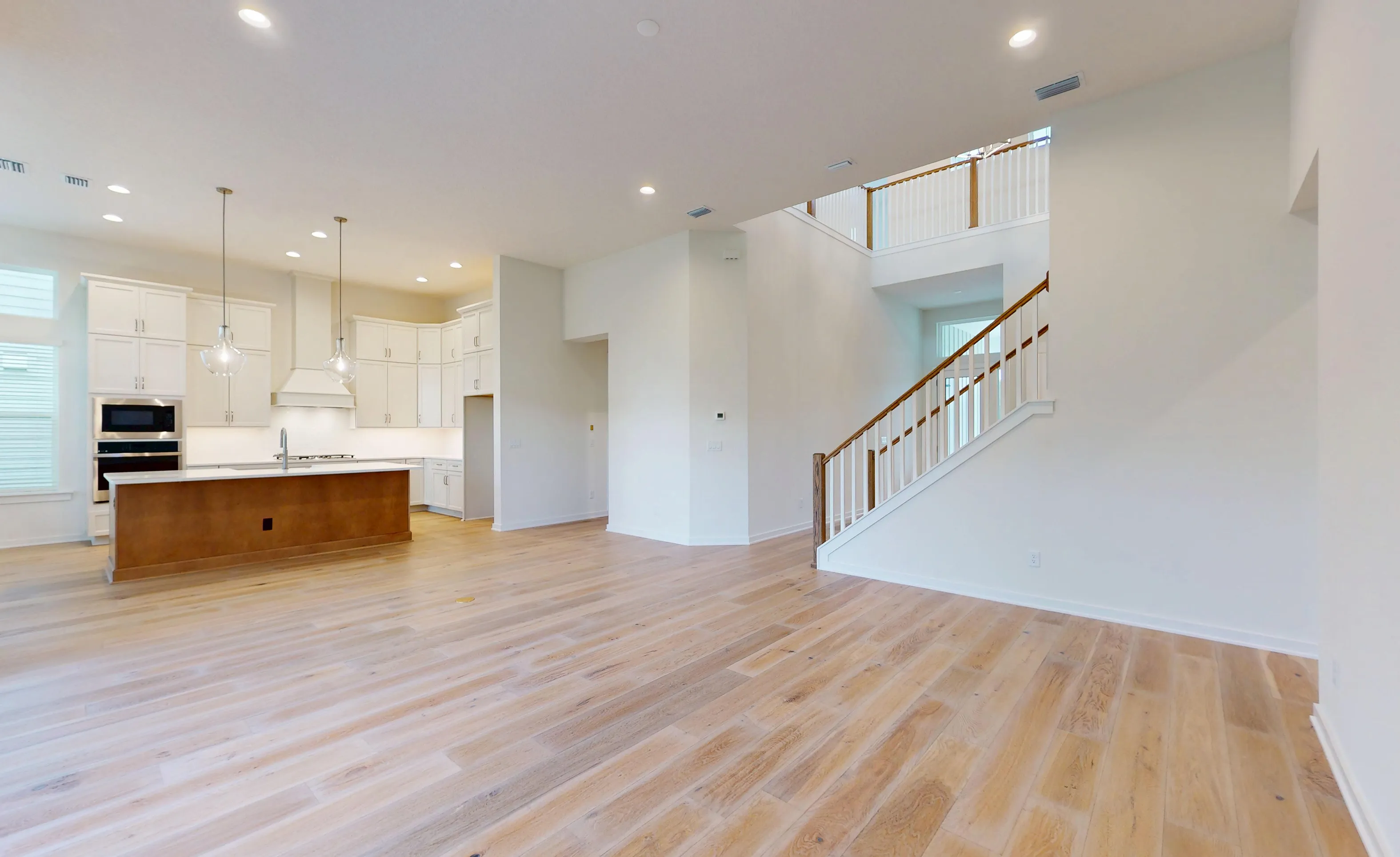 Living room and open kitchen in the Palos Verdes plan, featuring hardwood floors, a staircase, and white cabinetry.