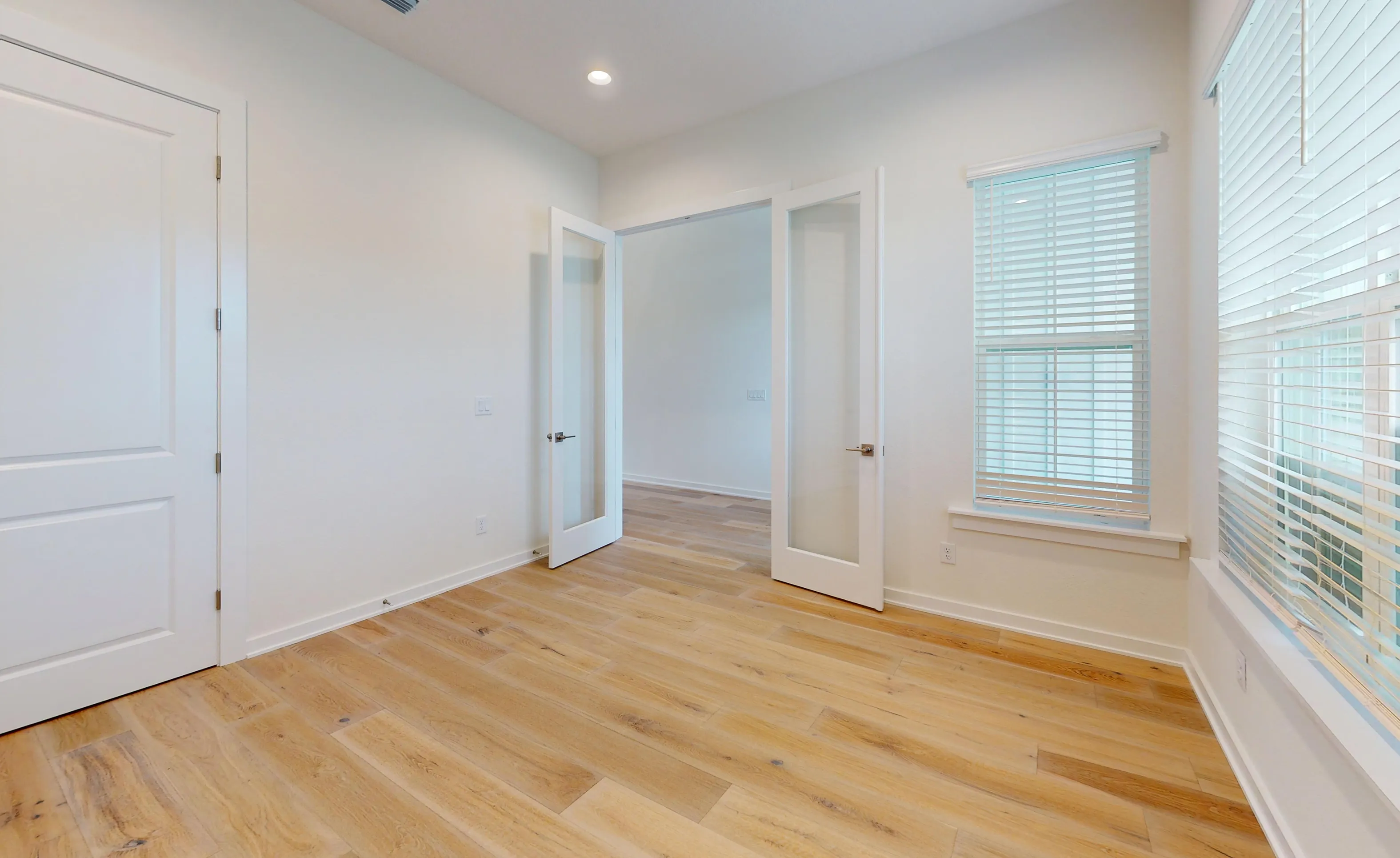 Home office in the Palos Verdes plan featuring wood-look floors, white walls, and glass-paneled double doors.