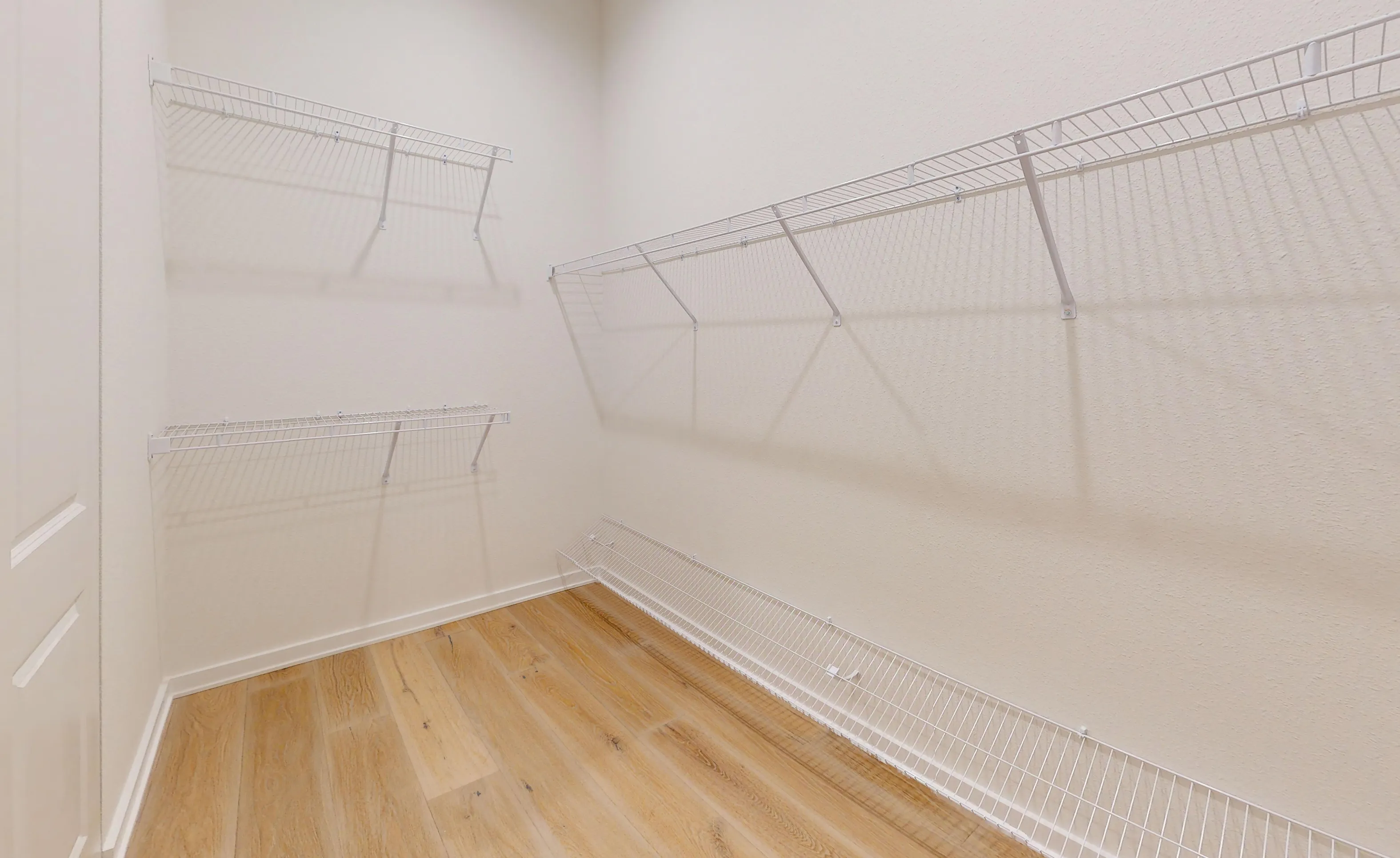 Walk-in closet of the Palos Verdes plan with beige walls, light wood-look flooring, and white wire shelving.