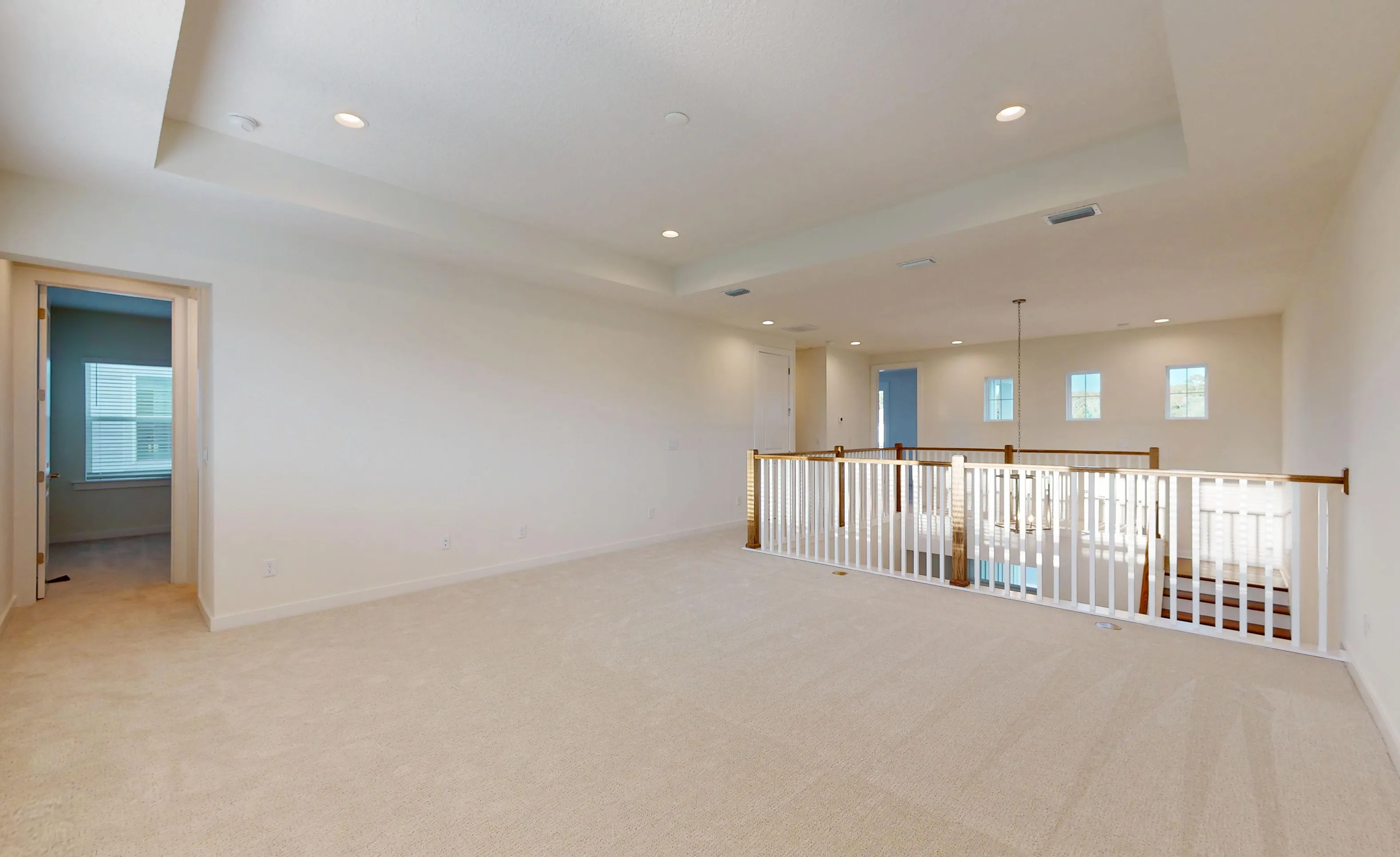 Spacious bonus room in the Palos Verdes plan with cream carpet, a tray ceiling, and a white balustrade overlooking the stairs.