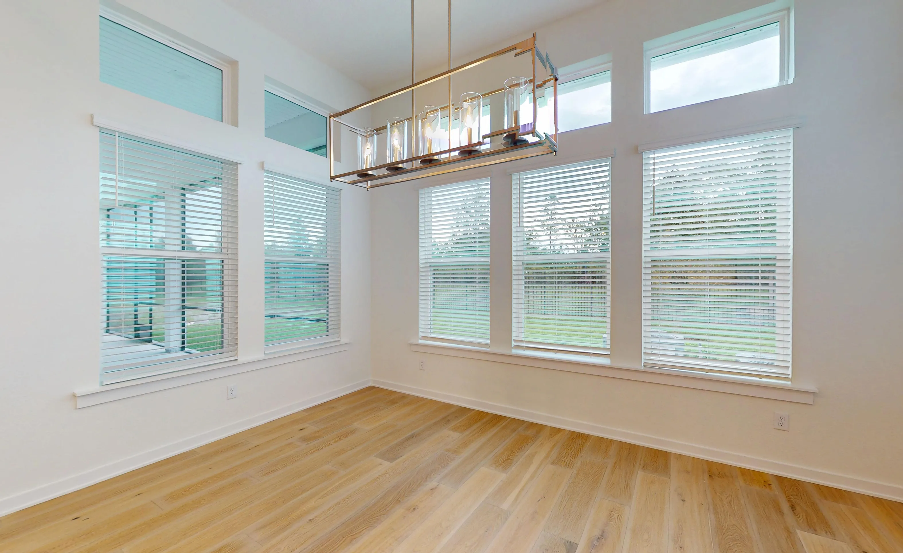 Breakfast nook with light wood floors, large windows with white blinds, and a rectangular gold-tone pendant light fixture.