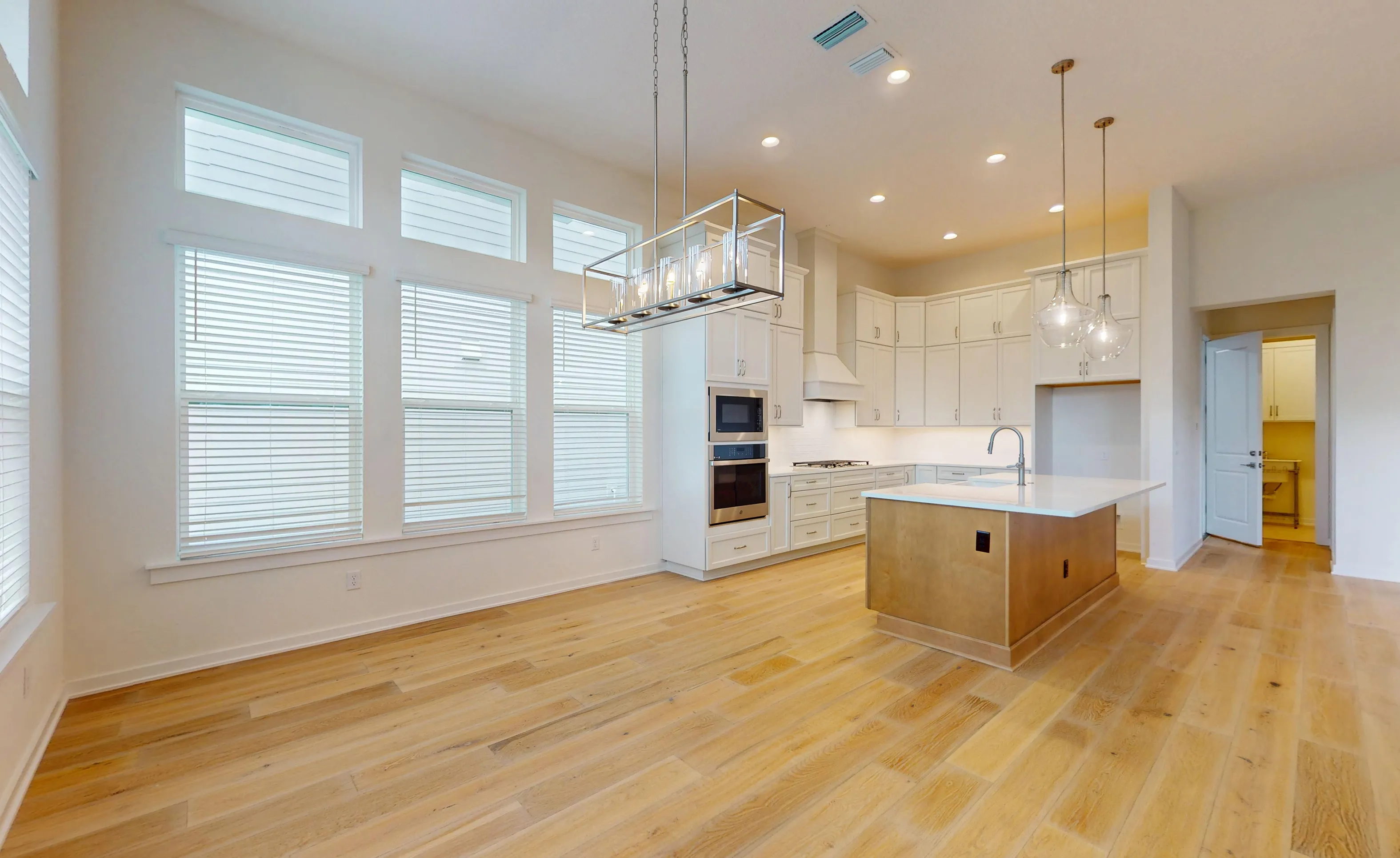 Kitchen with white cabinetry, a wood-toned island, light hardwood floors, and a large rectangular hanging light fixture.