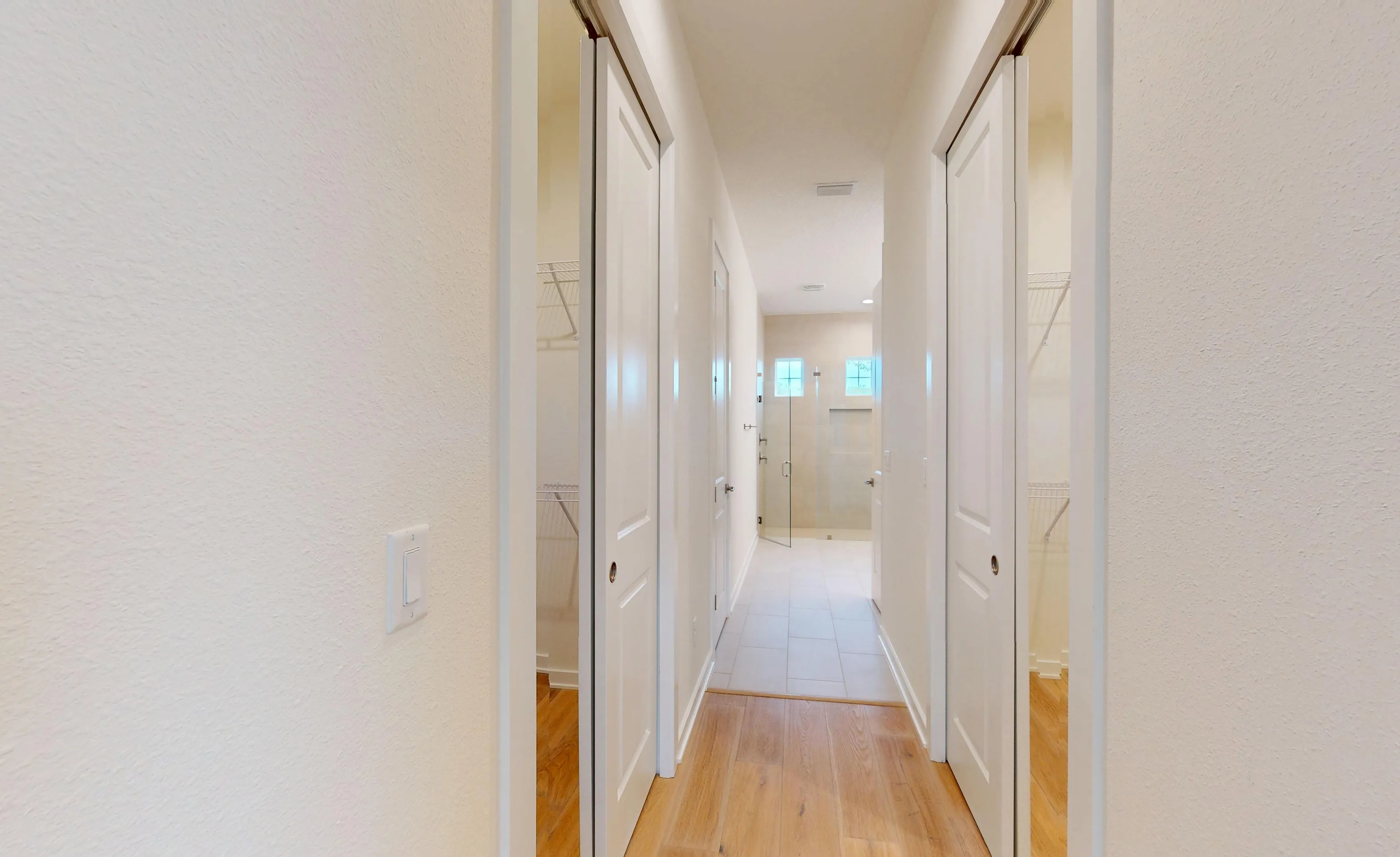Walk-in closet hallway with white doors, wire shelving, wood-look flooring, and a view into a tiled bathroom.