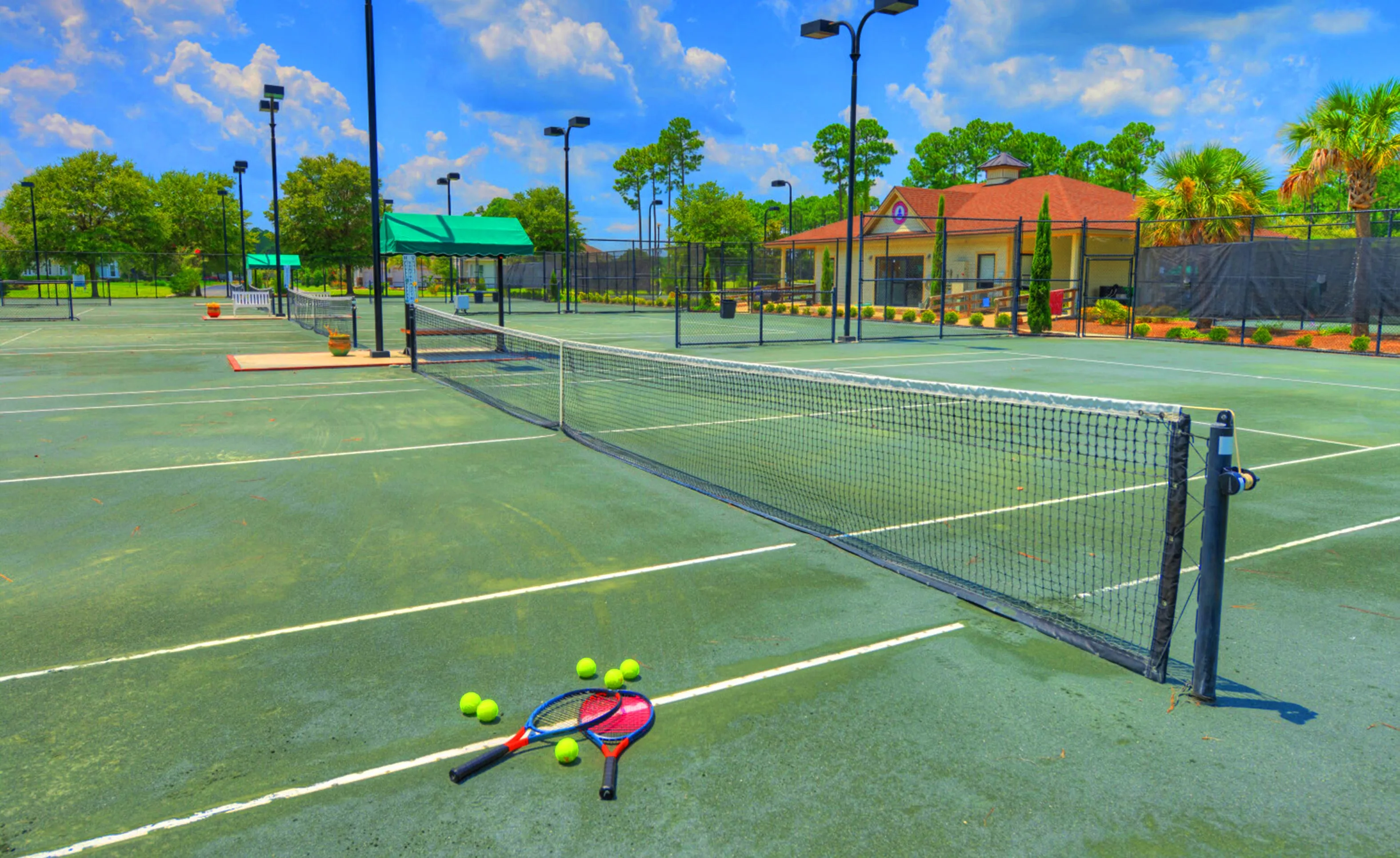 Tennis courts at Amelia National with rackets and balls in the foreground and a clubhouse building in the background.