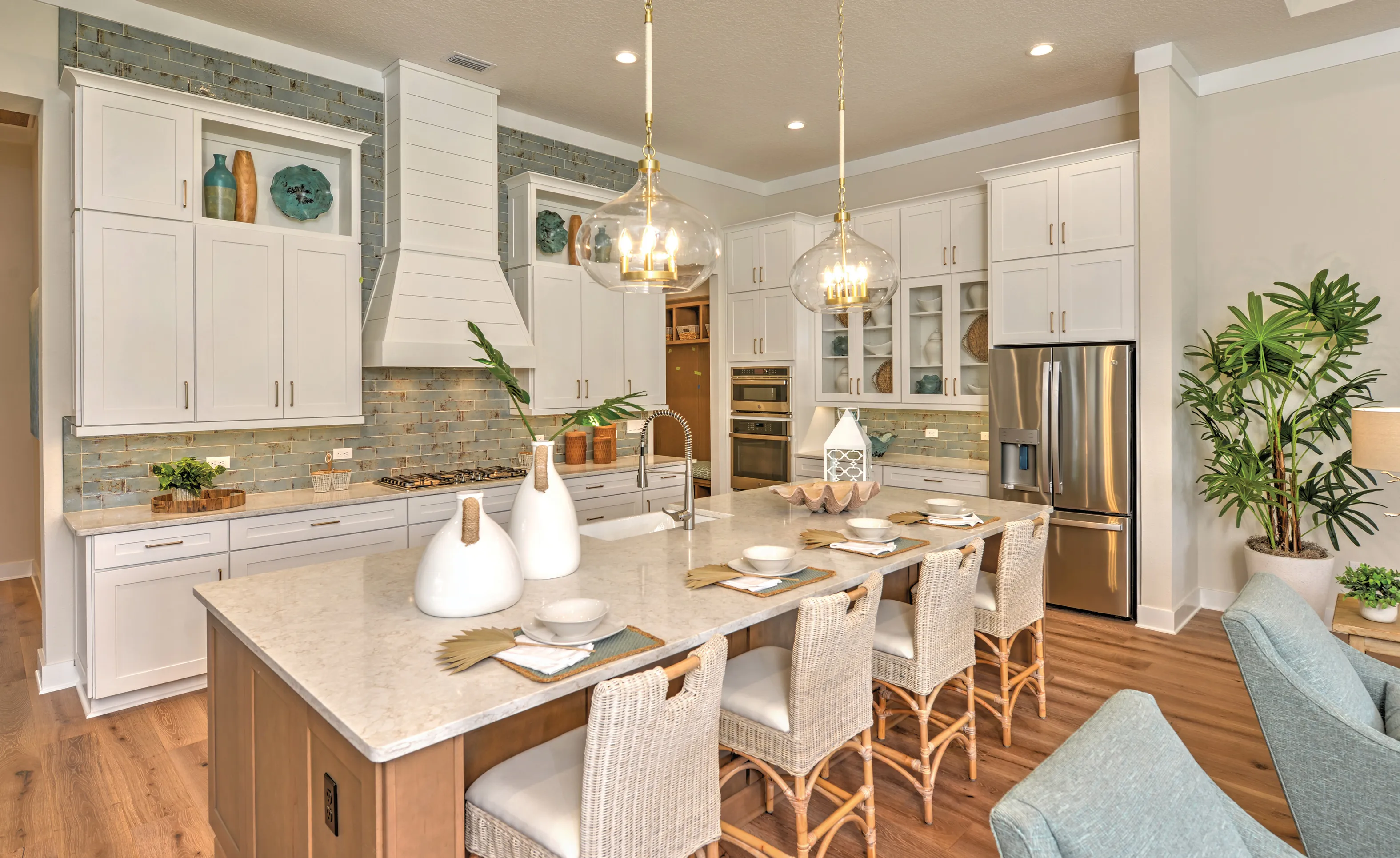 Kitchen in Amelia National with white cabinets, blue-gray tile backsplash, large center island, and stainless appliances.
