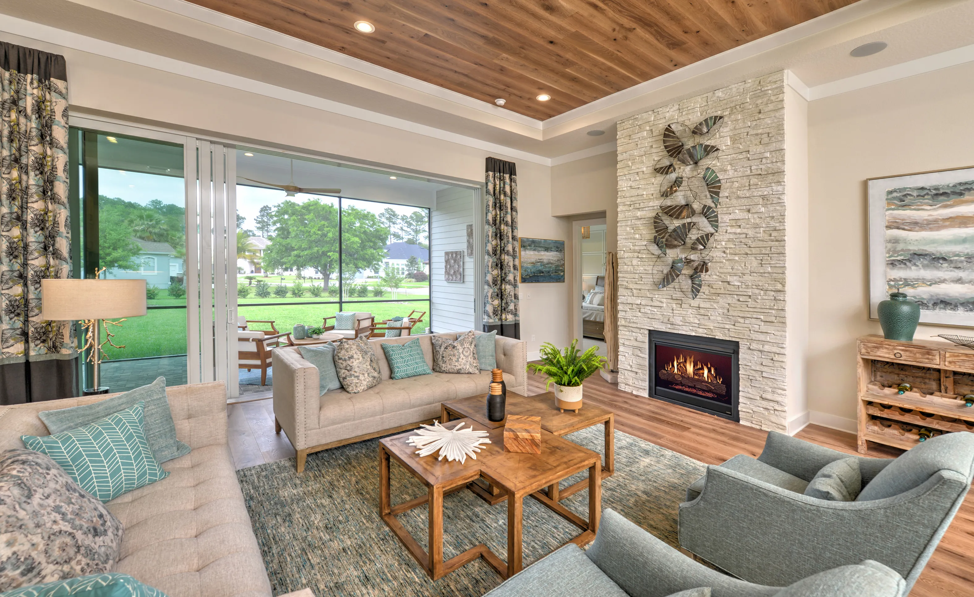 Living room at Amelia National with a stacked stone fireplace, wood-paneled tray ceiling, and sliding glass doors to patio.