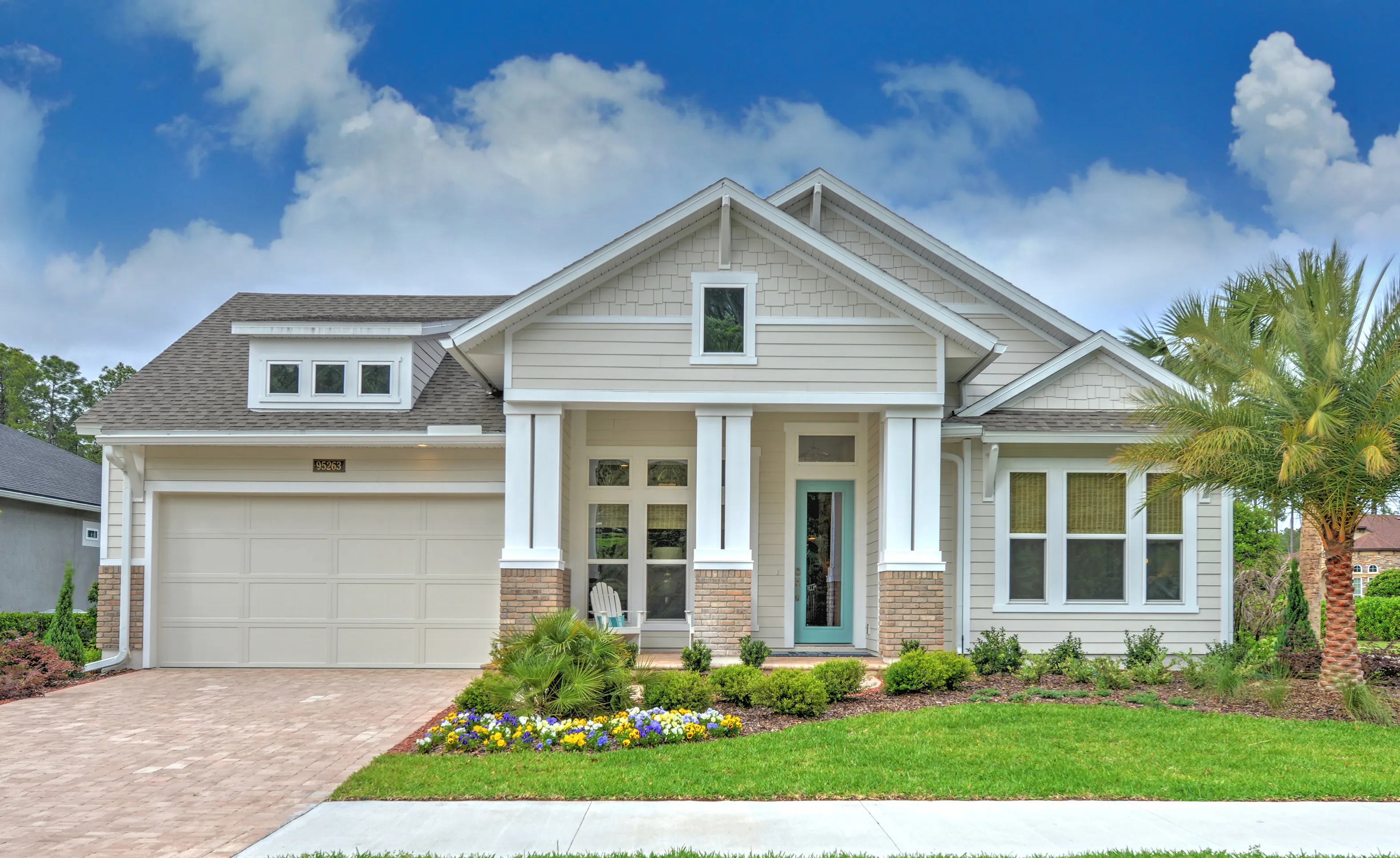 Exterior view of a beige coastal home in Amelia National with a teal front door, brick columns, and paved driveway.
