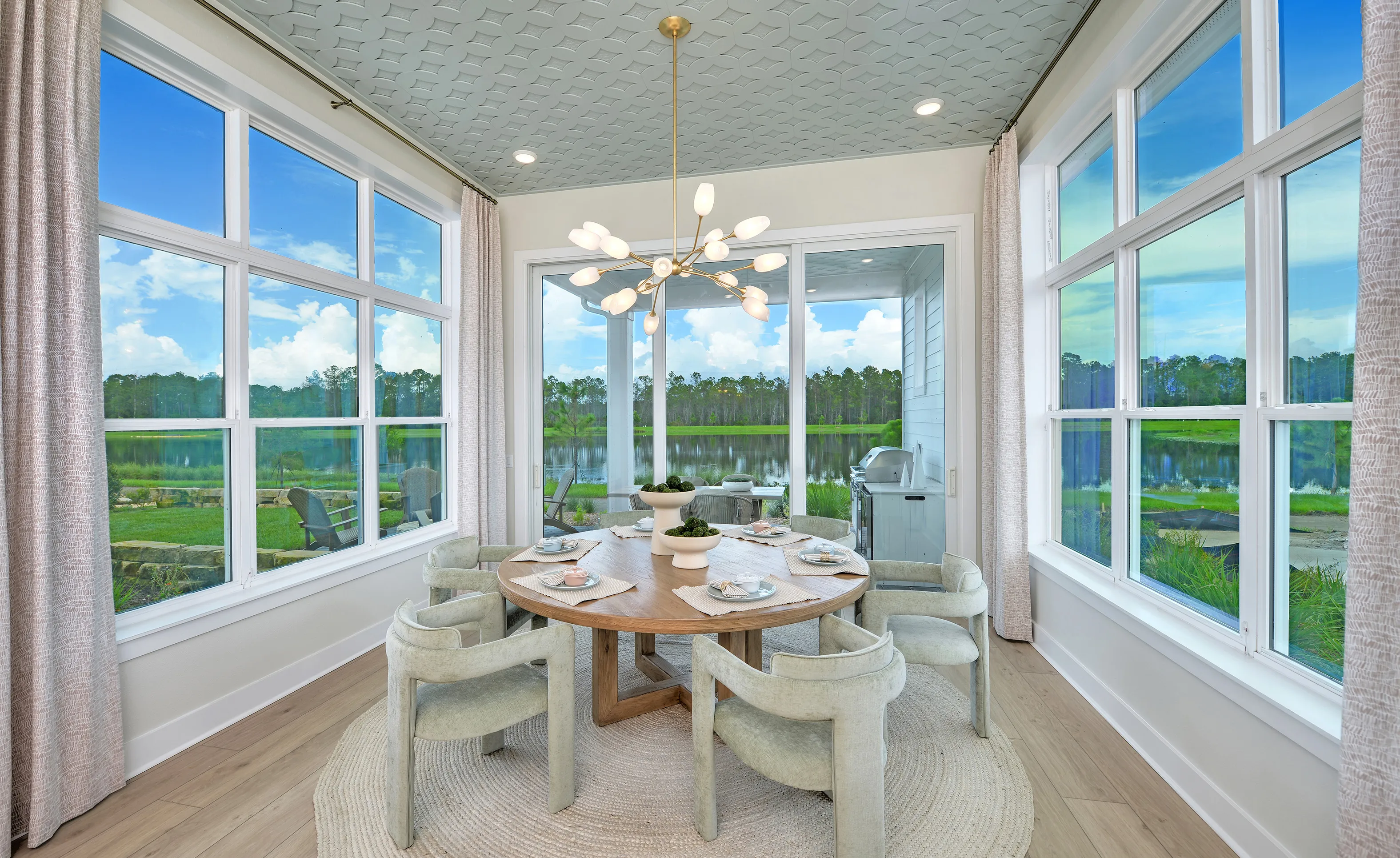 Dining Room with wood table, upholstered chairs, globe chandelier, and blue patterned ceiling, overlooking a lake.