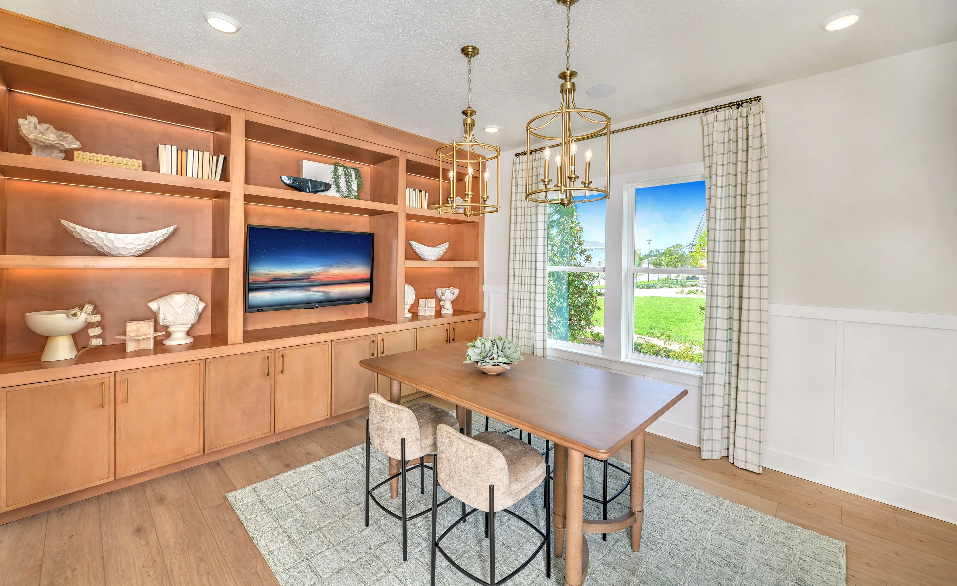 Study in the Brooklyn plan with a large wooden wall unit, two gold pendant lights, a table, and plaid curtains.