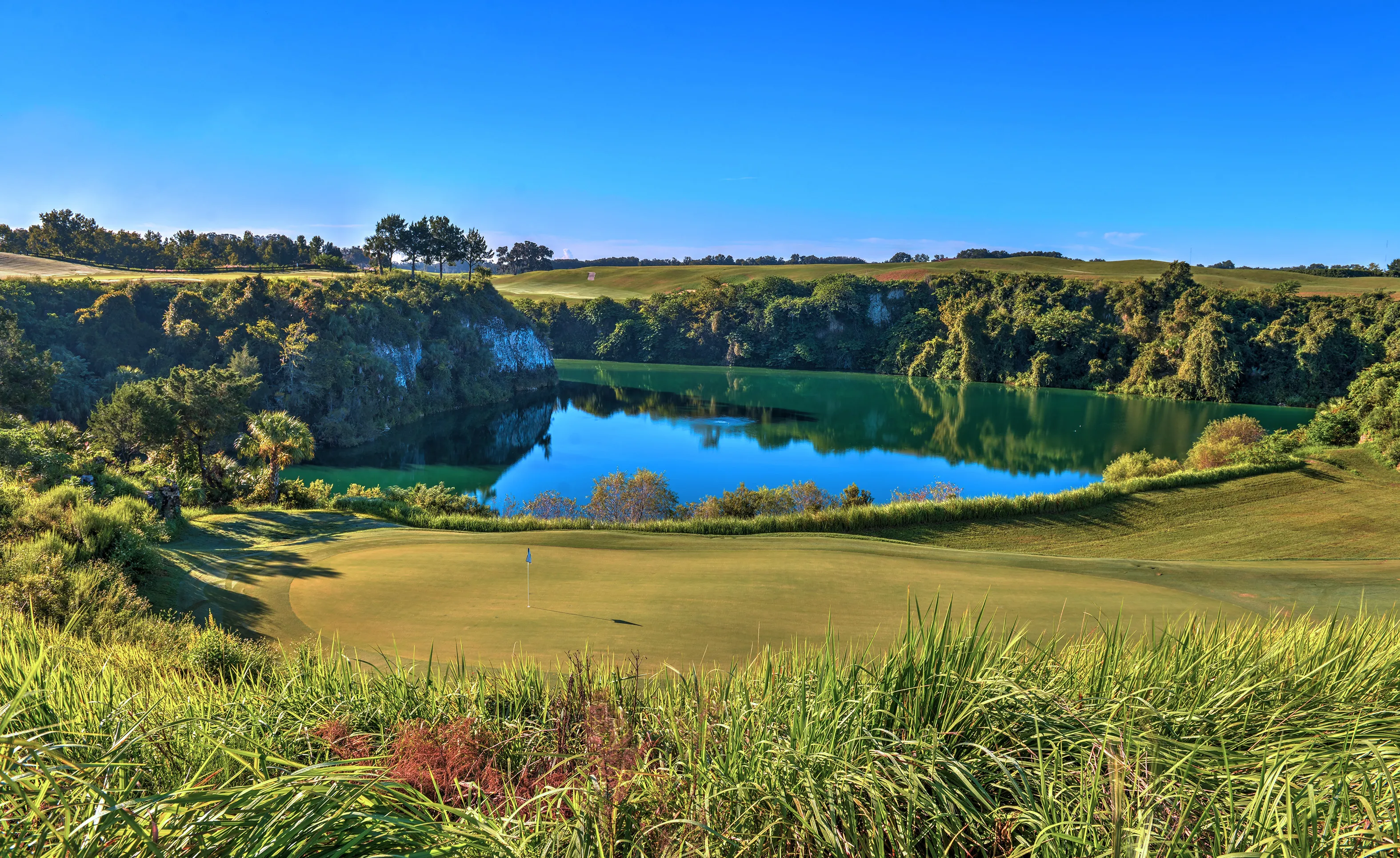 Golf course green overlooking a deep quarry pond surrounded by rocky cliffs and lush vegetation at IronCrest.