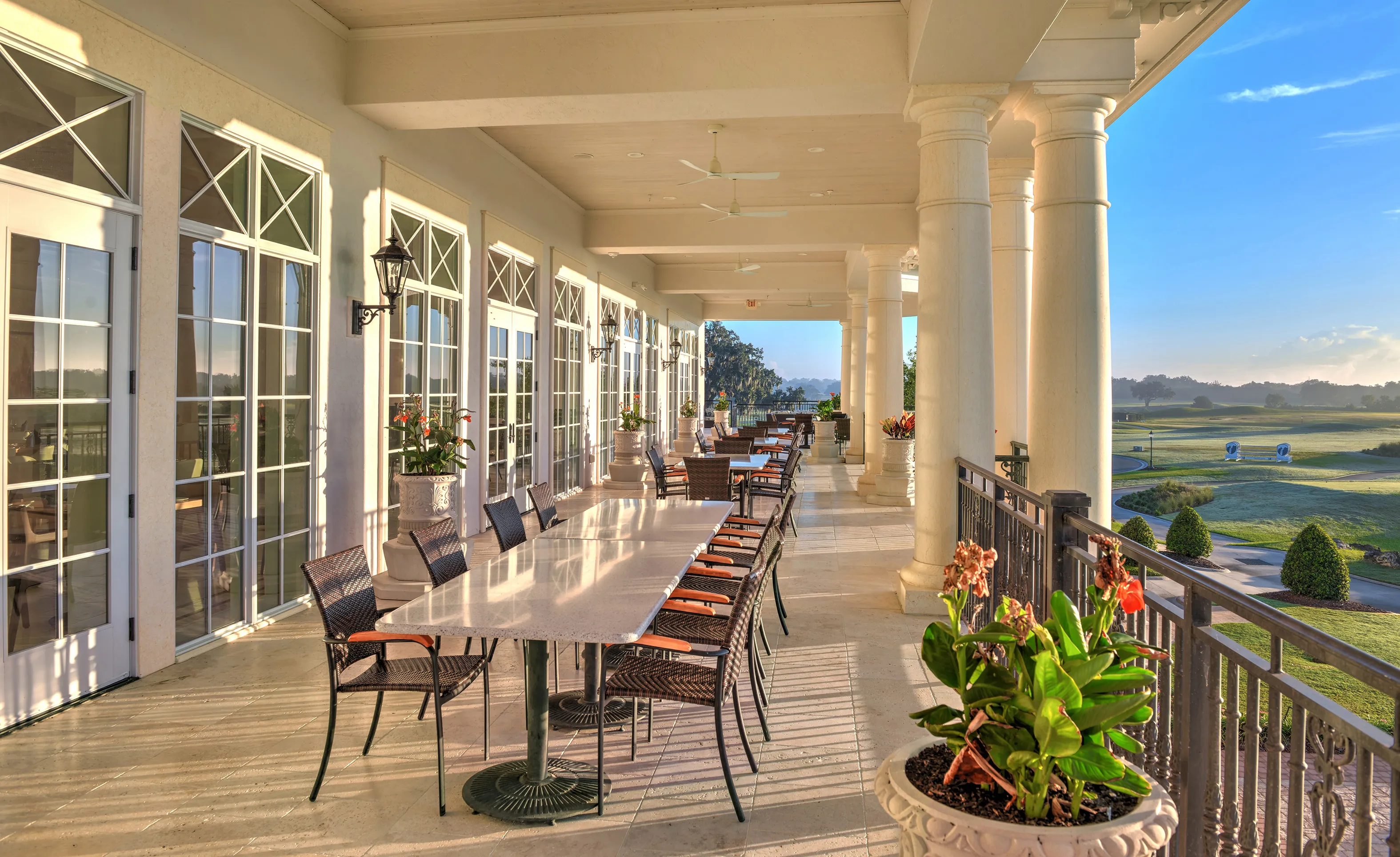 Covered outdoor patio at IronCrest with rows of dining tables, tall white columns, and views of a golf course.