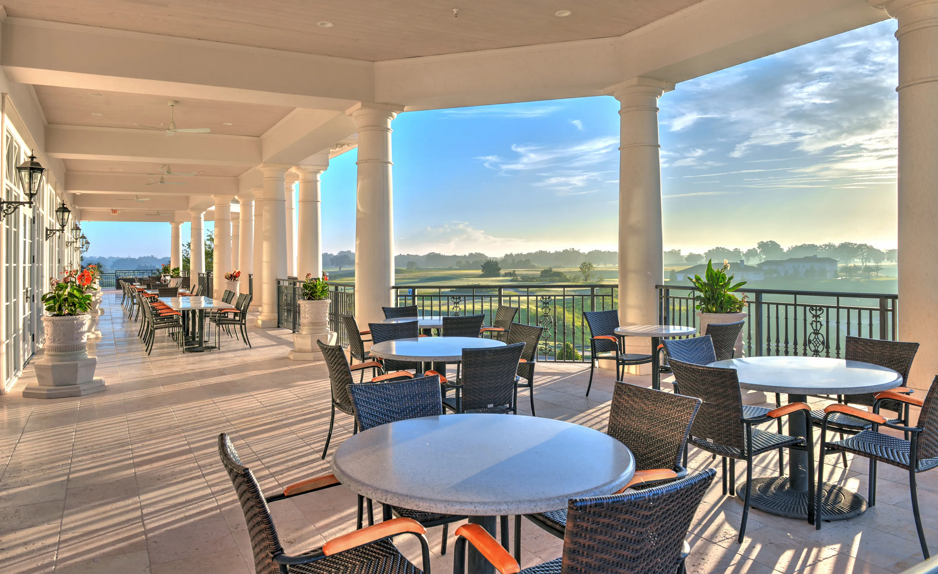 Covered patio at IronCrest with white columns, tile flooring, and wicker dining sets overlooking a green golf course landscape.