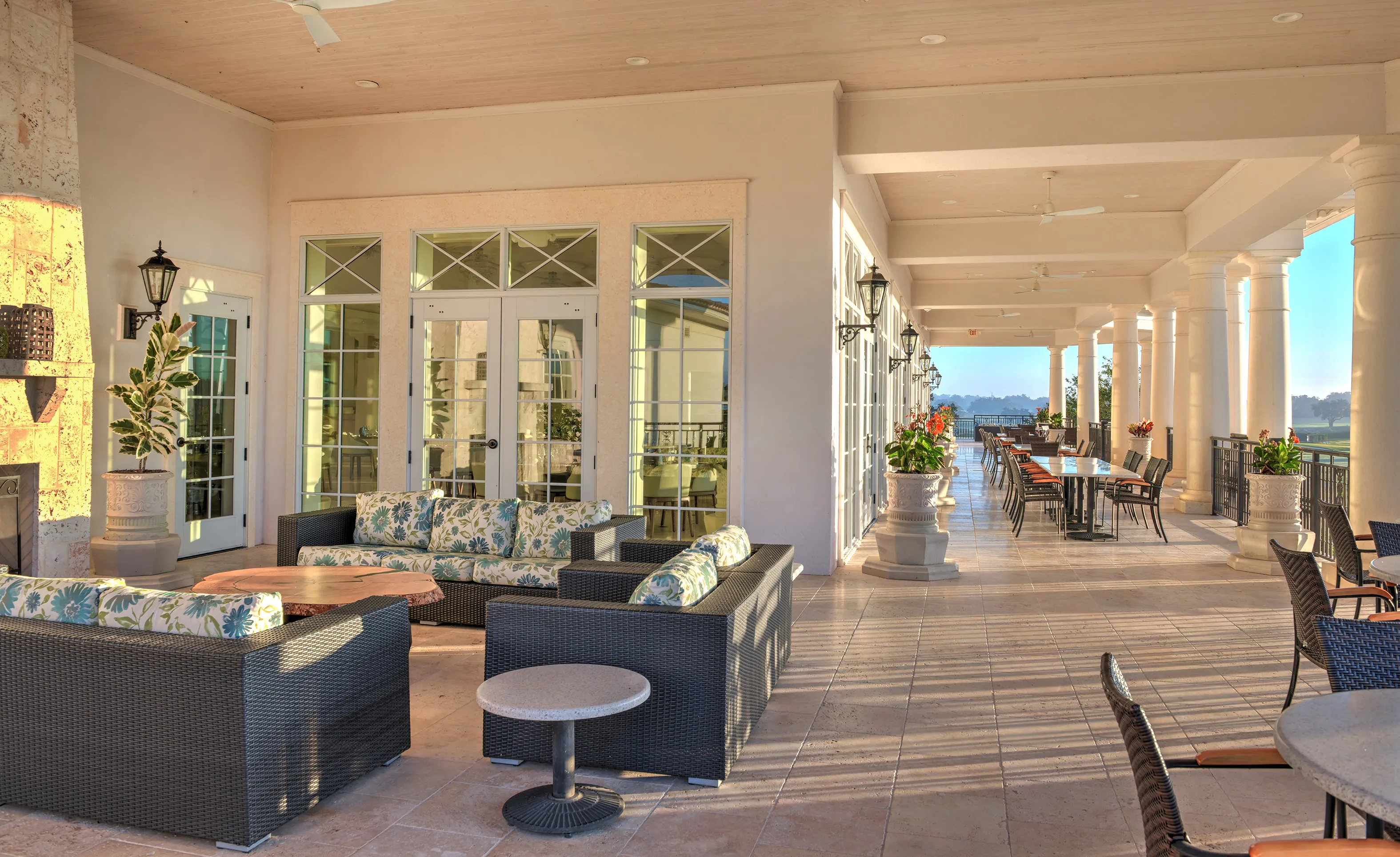 Covered patio at IronCrest with tiled flooring, wicker outdoor furniture, stone columns, and distant golf course views.