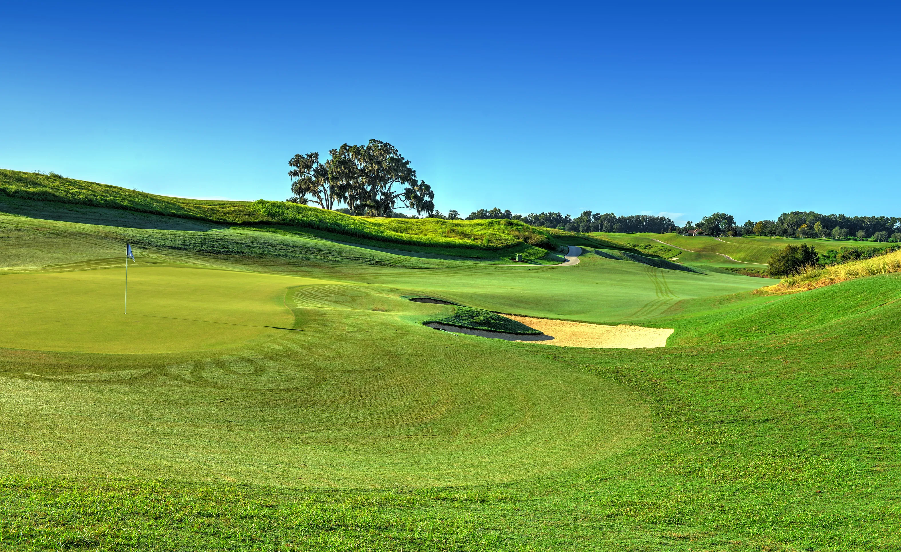Golf course putting green with a flag and sand bunker, surrounded by rolling hills and trees at IronCrest.