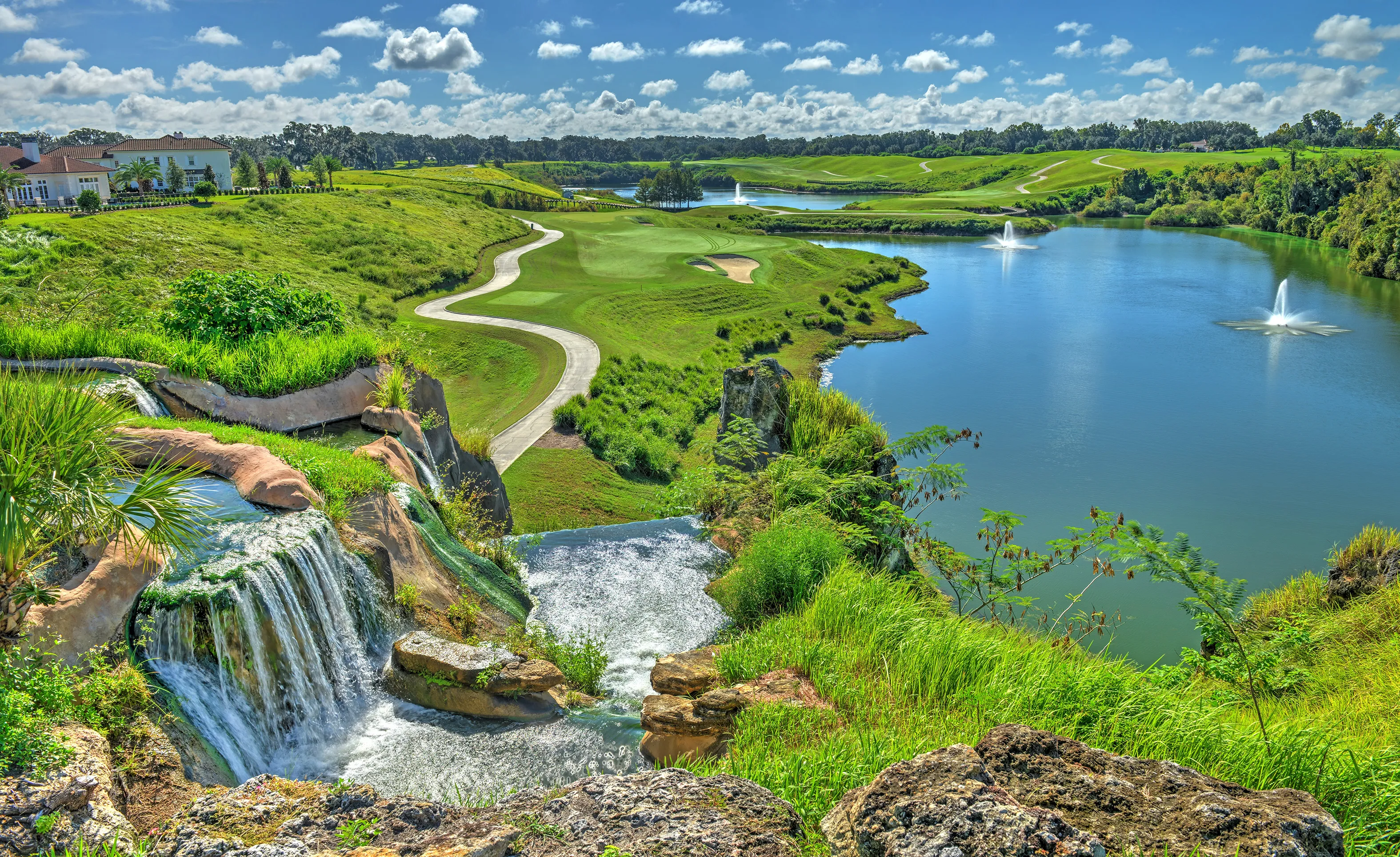 Scenic view of the IronCrest community featuring a tiered rock waterfall overlooking a golf course, lake, and fountains.
