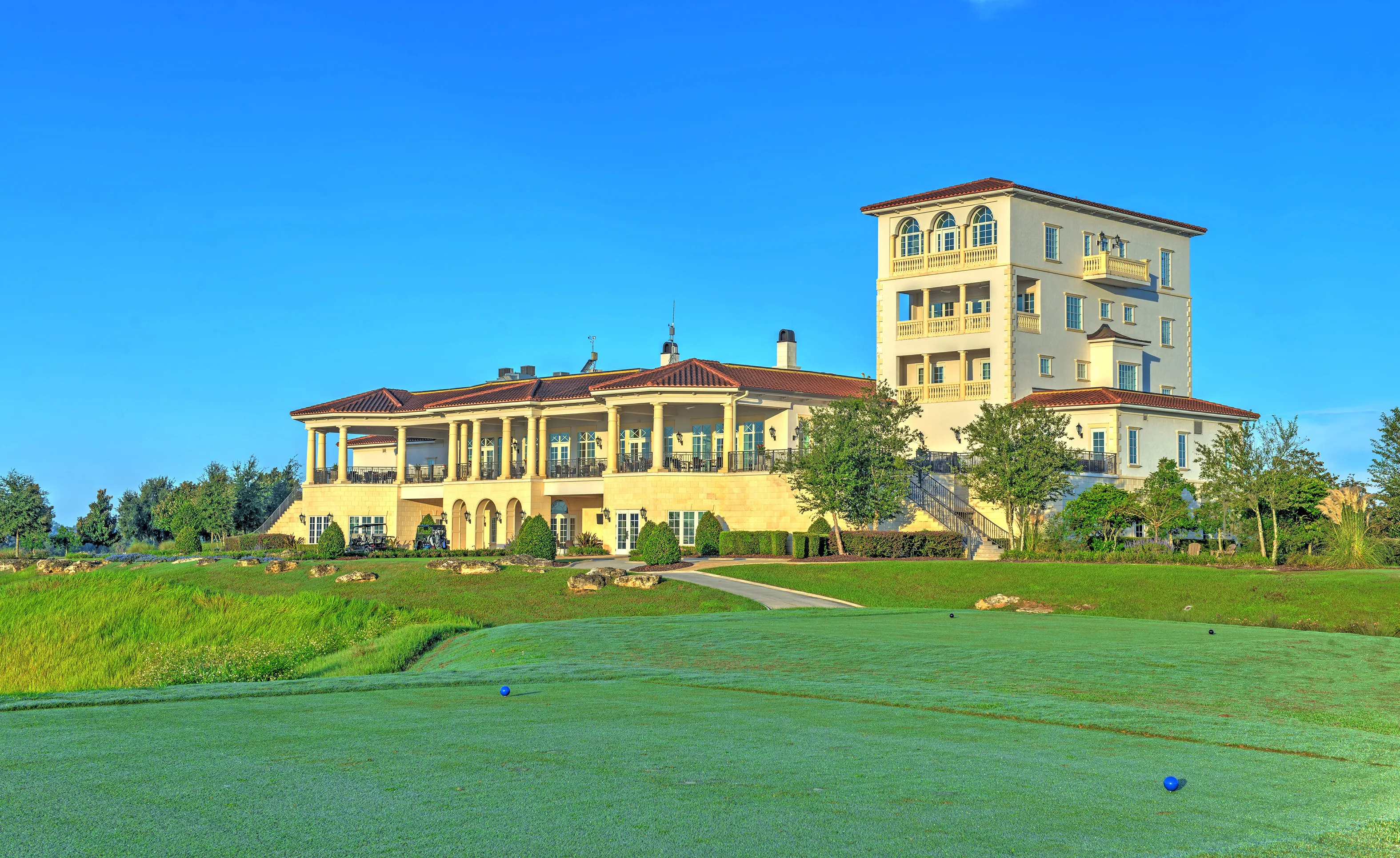 Exterior of a multi-story clubhouse at IronCrest with a terracotta tile roof, stone facade, and a tall tower.