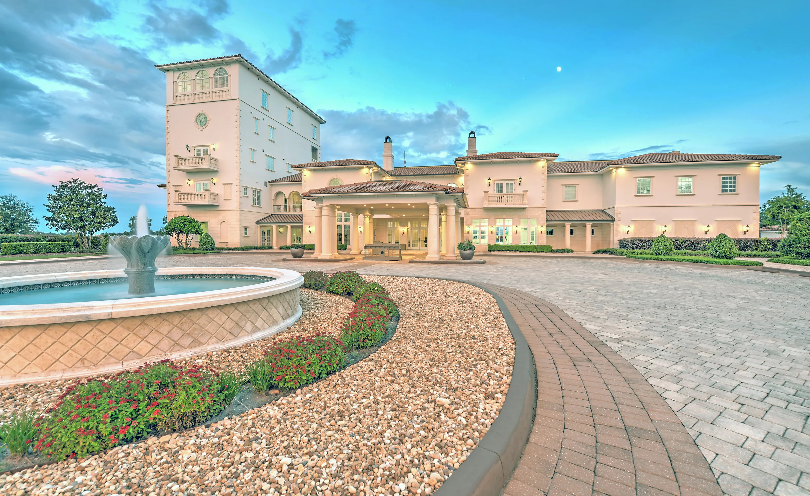 Exterior view of the IronCrest community clubhouse featuring a paved circular driveway, a stone fountain, and tall tower.