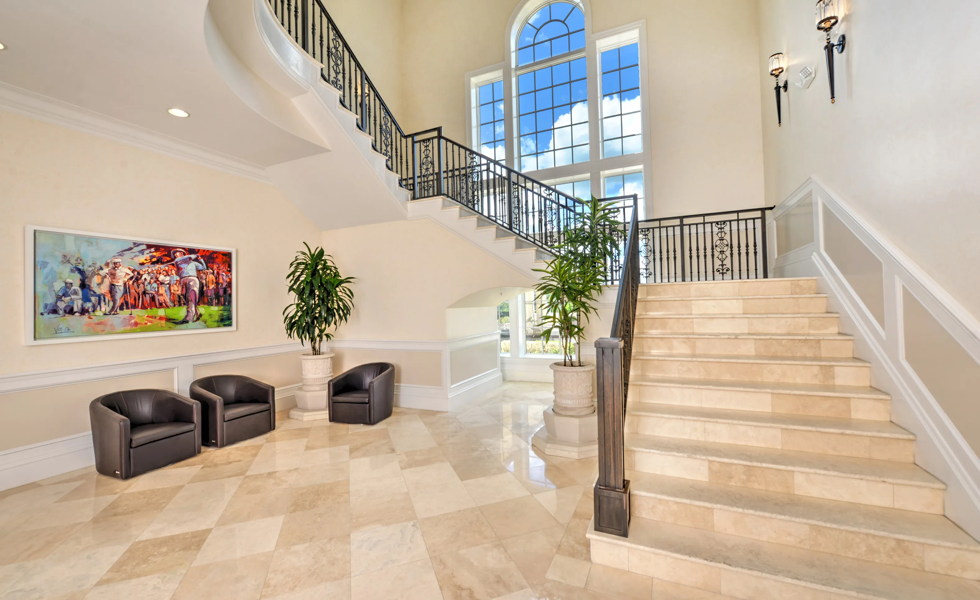 Grand entryway at IronCrest with a curved staircase, stone steps, wrought iron railing, two leather chairs, and large window.