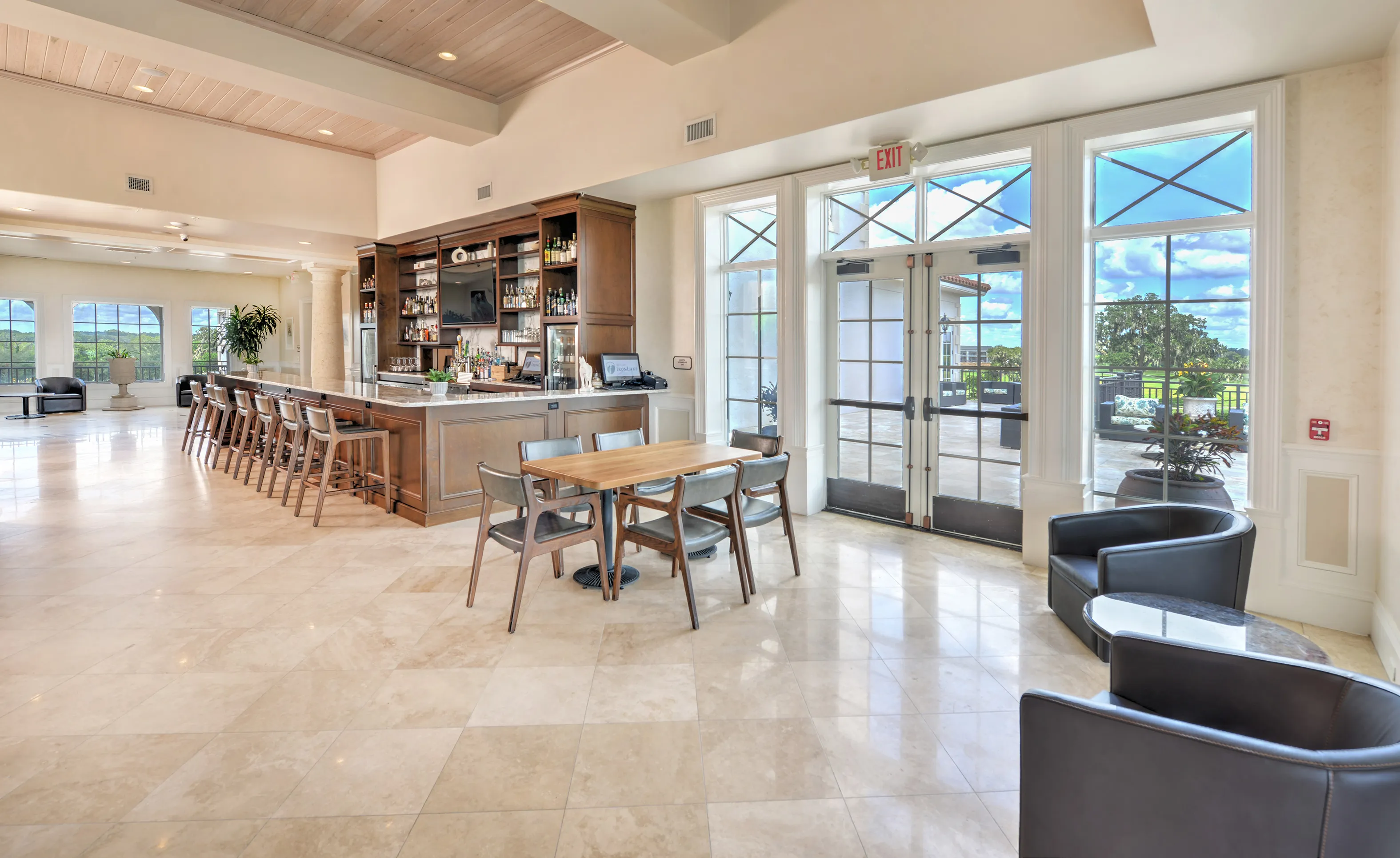 Spacious IronCrest clubhouse room featuring a wood bar, tile flooring, dining tables, and glass doors leading to a patio.