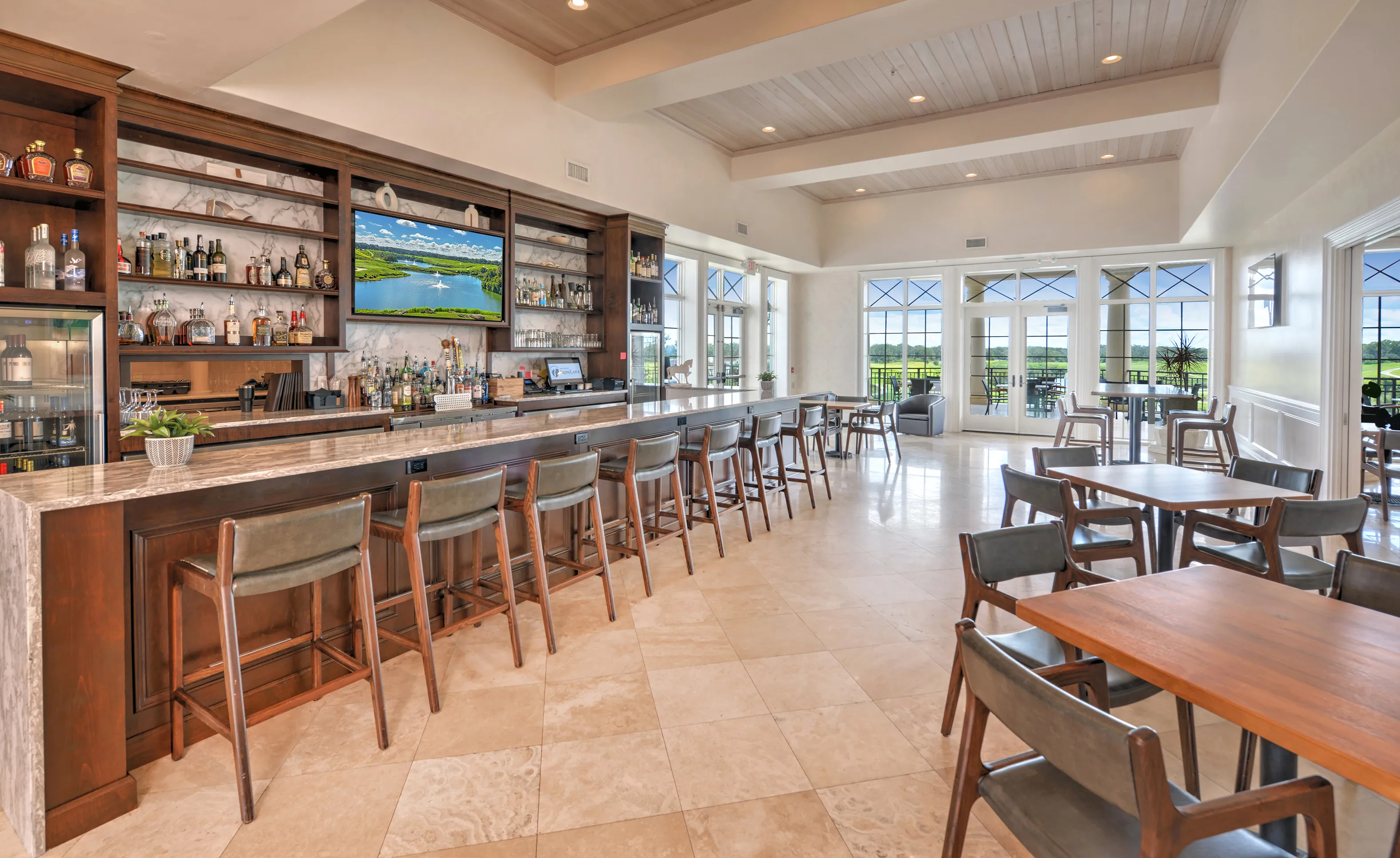 Bar area at IronCrest with a long counter, high-top chairs, wood cabinetry, marble backsplash, and large glass windows.