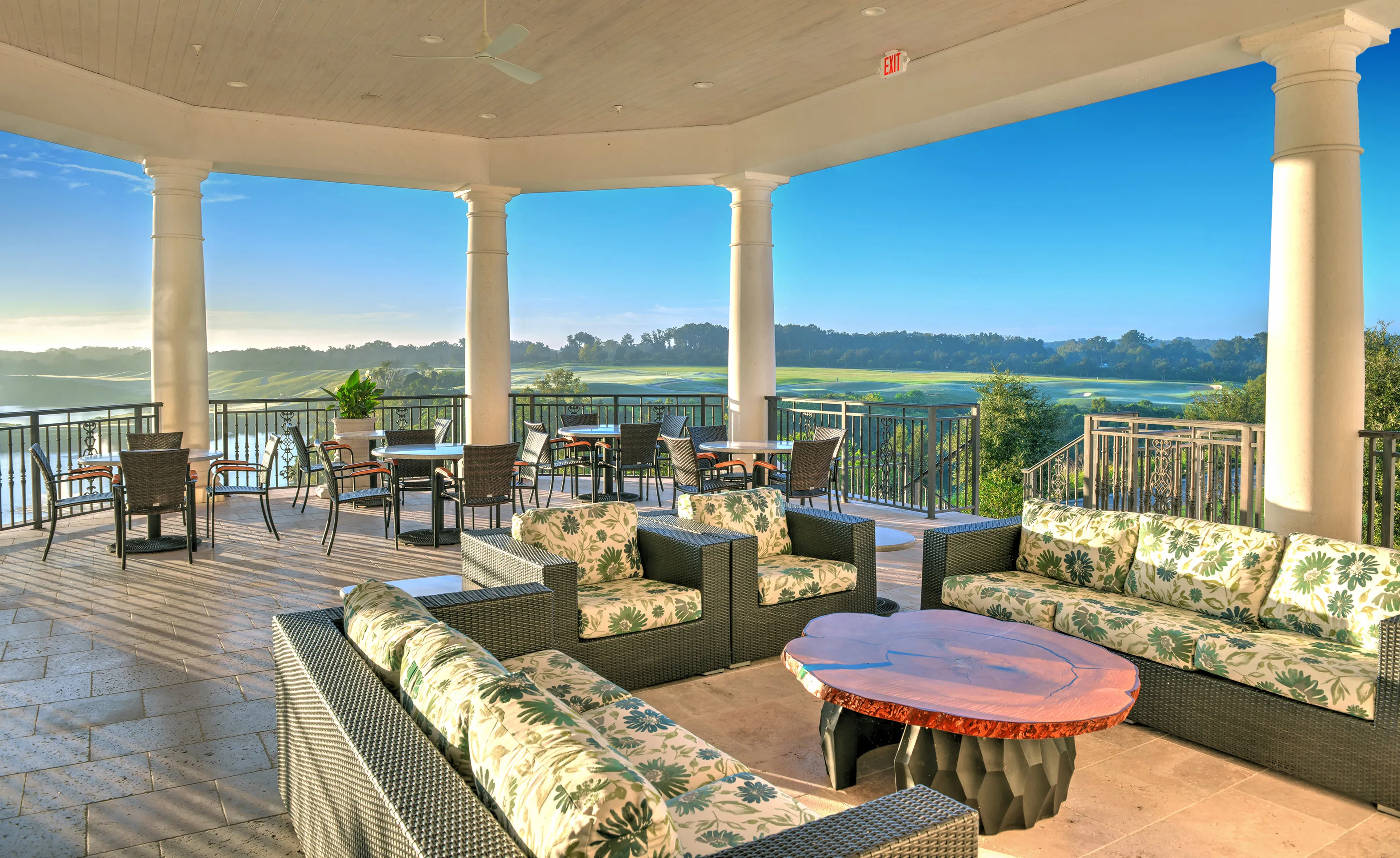 Covered patio at IronCrest with wicker seating, floral cushions, a wooden coffee table, and views of a golf course.