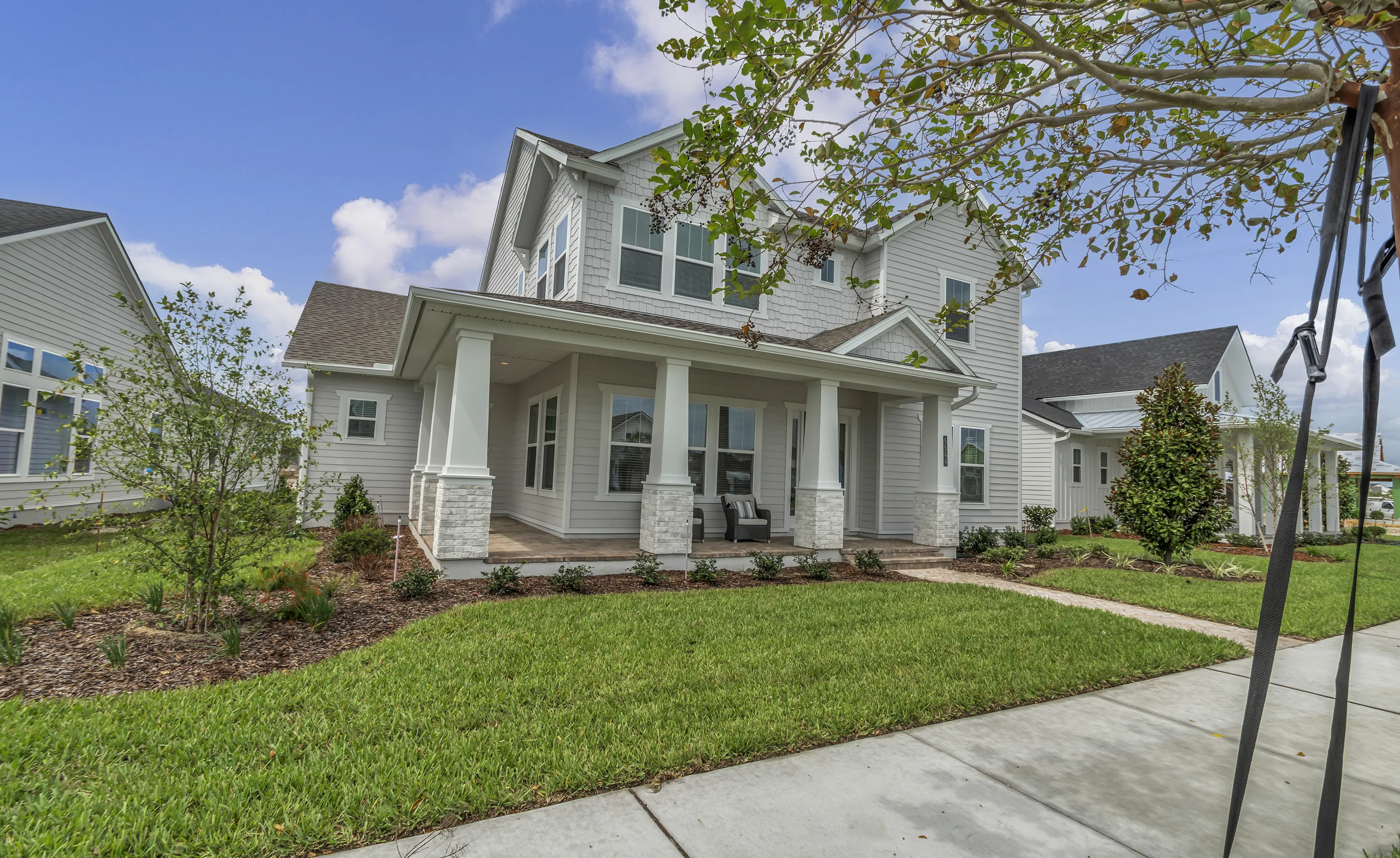 Front exterior of a gray two-story home with a covered front porch, white columns on stone bases, and shake siding.
