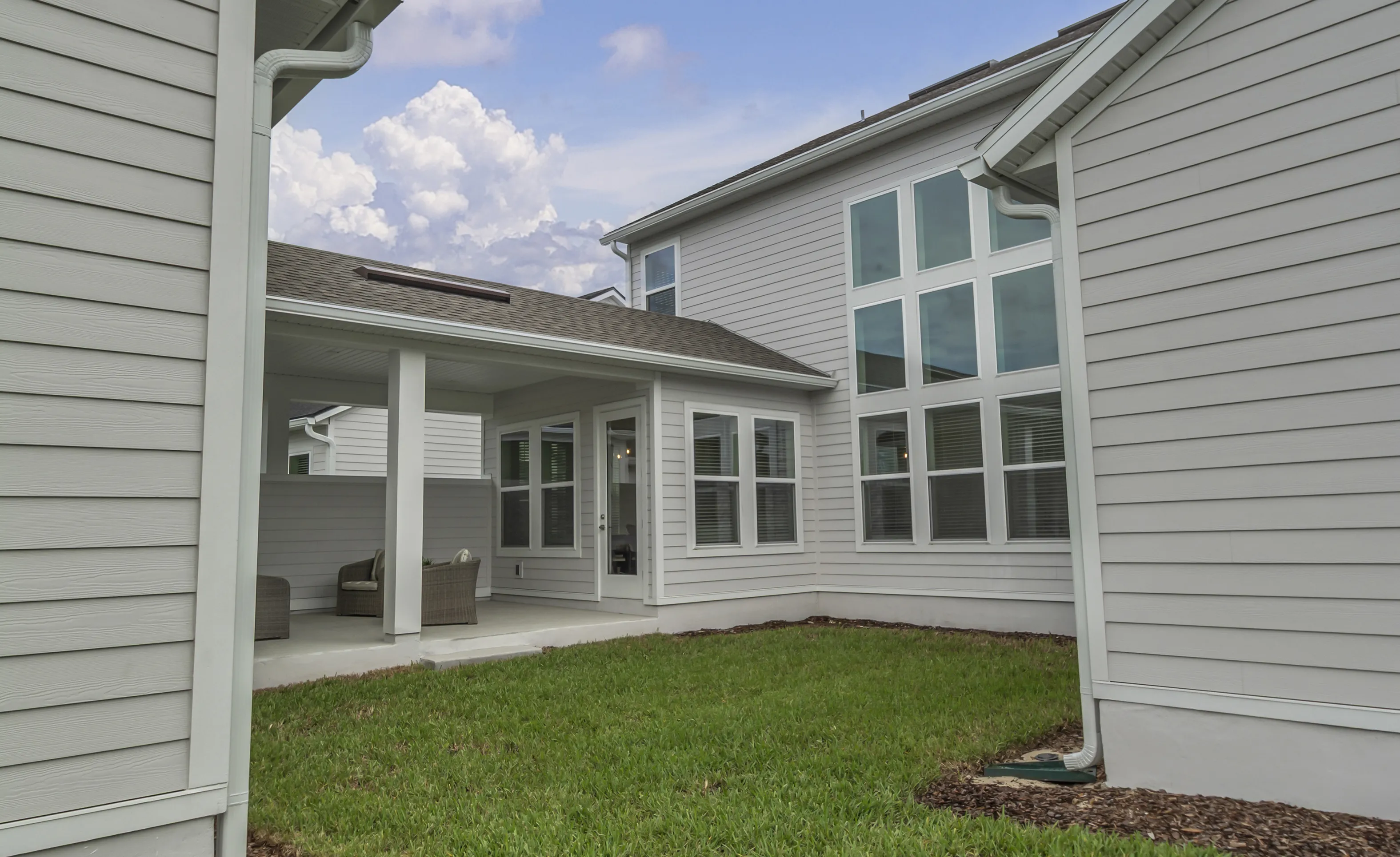 Rear exterior of Braddock home at Seven Pines featuring light gray siding, a covered patio, and tall floor-to-ceiling windows.