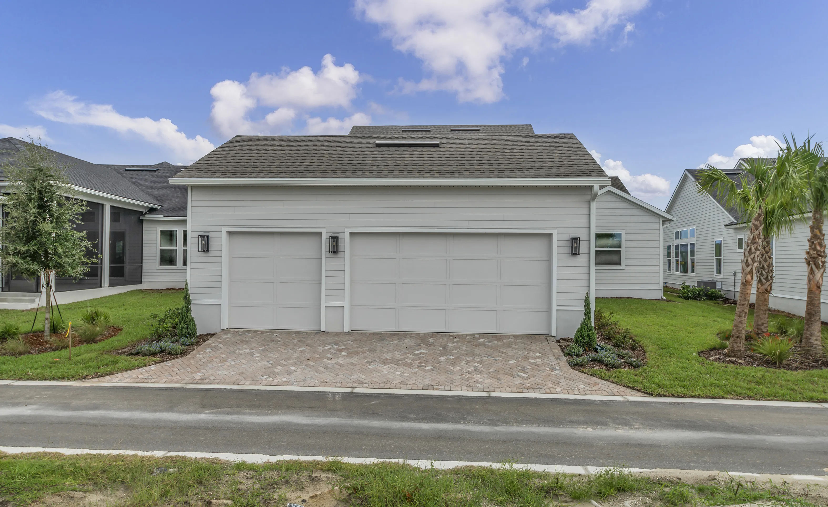 Exterior view of the Braddock plan garage at Seven Pines with gray siding, a paved driveway, and palm trees in the yard.