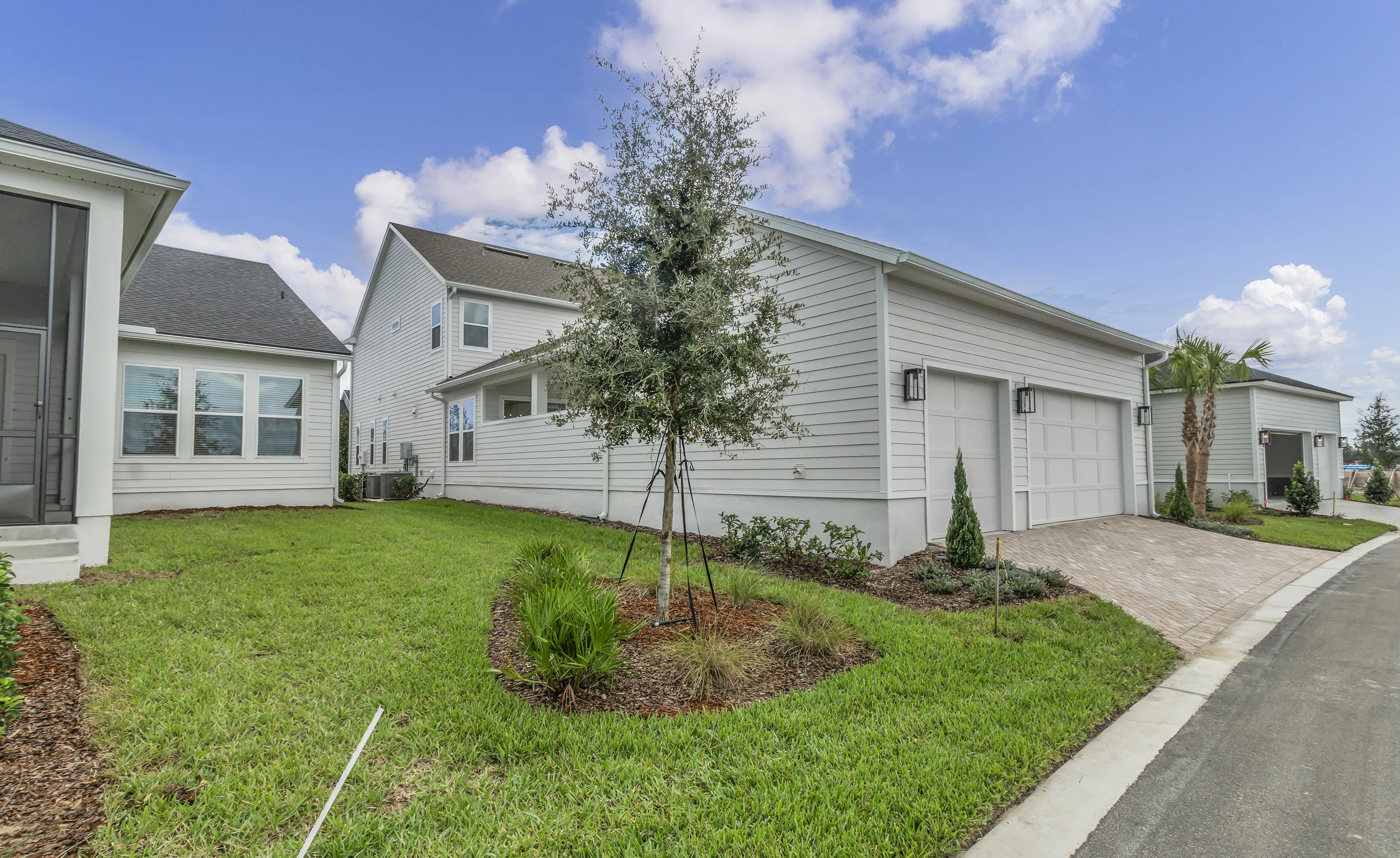 Side exterior view of a Braddock plan home at Seven Pines featuring light gray horizontal siding, a paver driveway, and lawn.