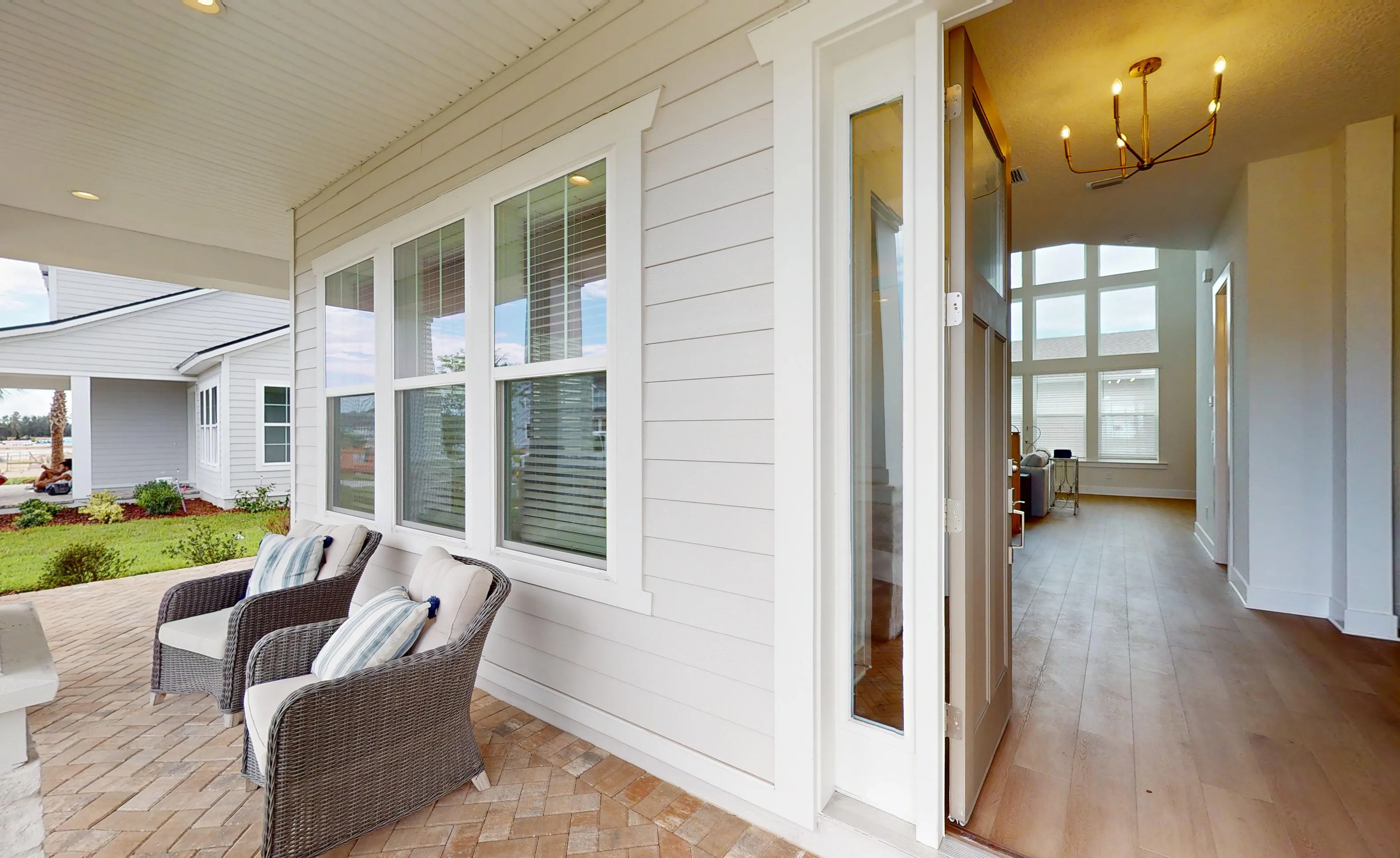 Covered porch of the Braddock plan with wicker chairs, brick-patterned floor, and view through an open door into the home.