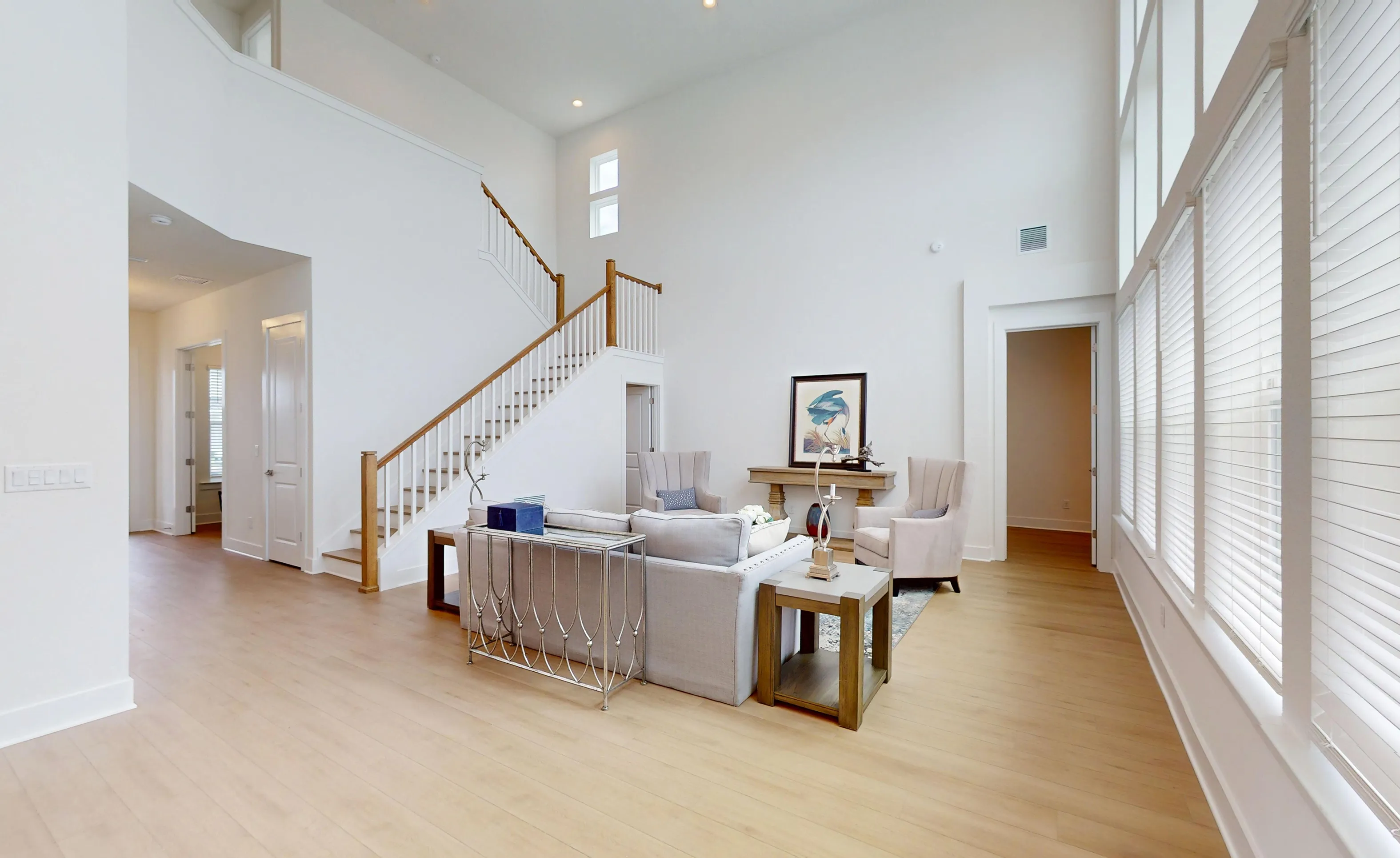 Braddock plan living room with high ceilings, wood flooring, a staircase with white railings, and tall windows with blinds.
