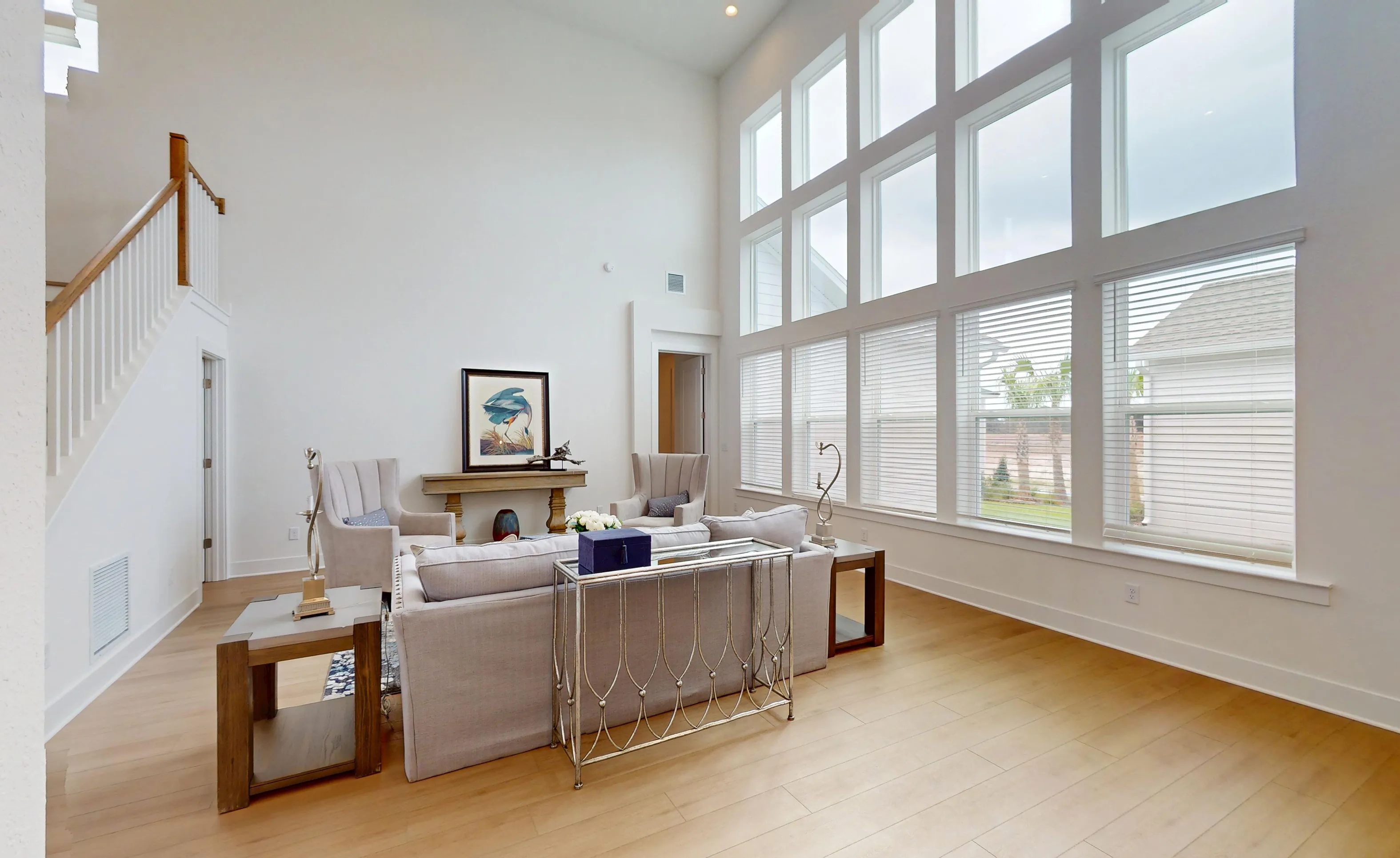 Living room in Braddock plan with tall ceilings, large windows, wood floors, and a staircase with white railings.